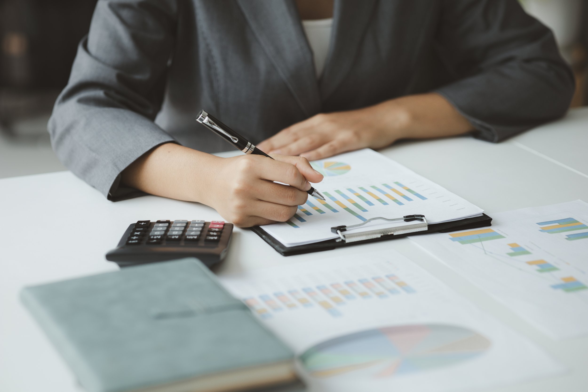 Person in a gray blazer working with financial graphs, charts, and a calculator on a white desk