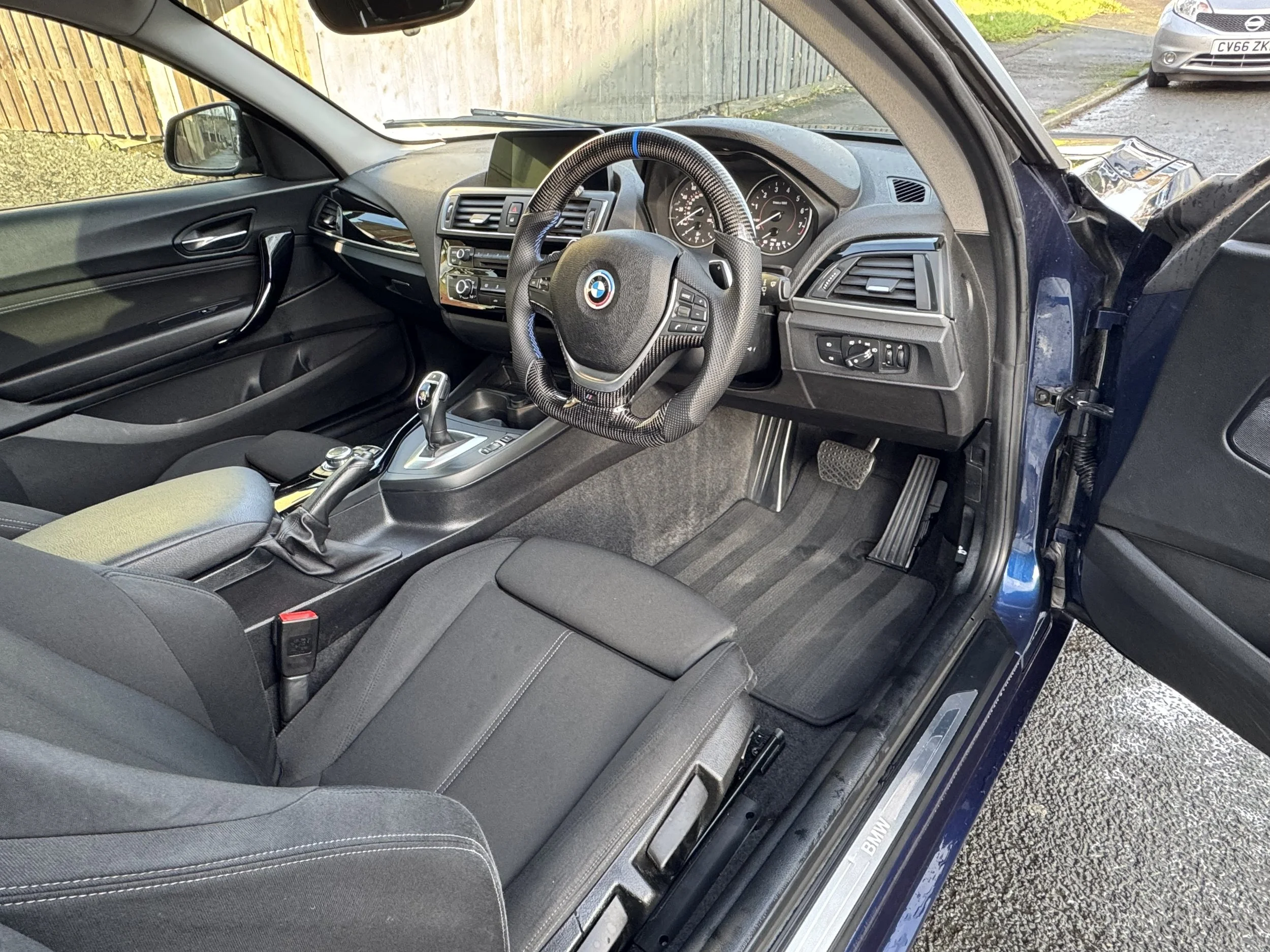 Interior of a BMW car showing the driver's side with a steering wheel, dashboard, gear shift, and front seat.