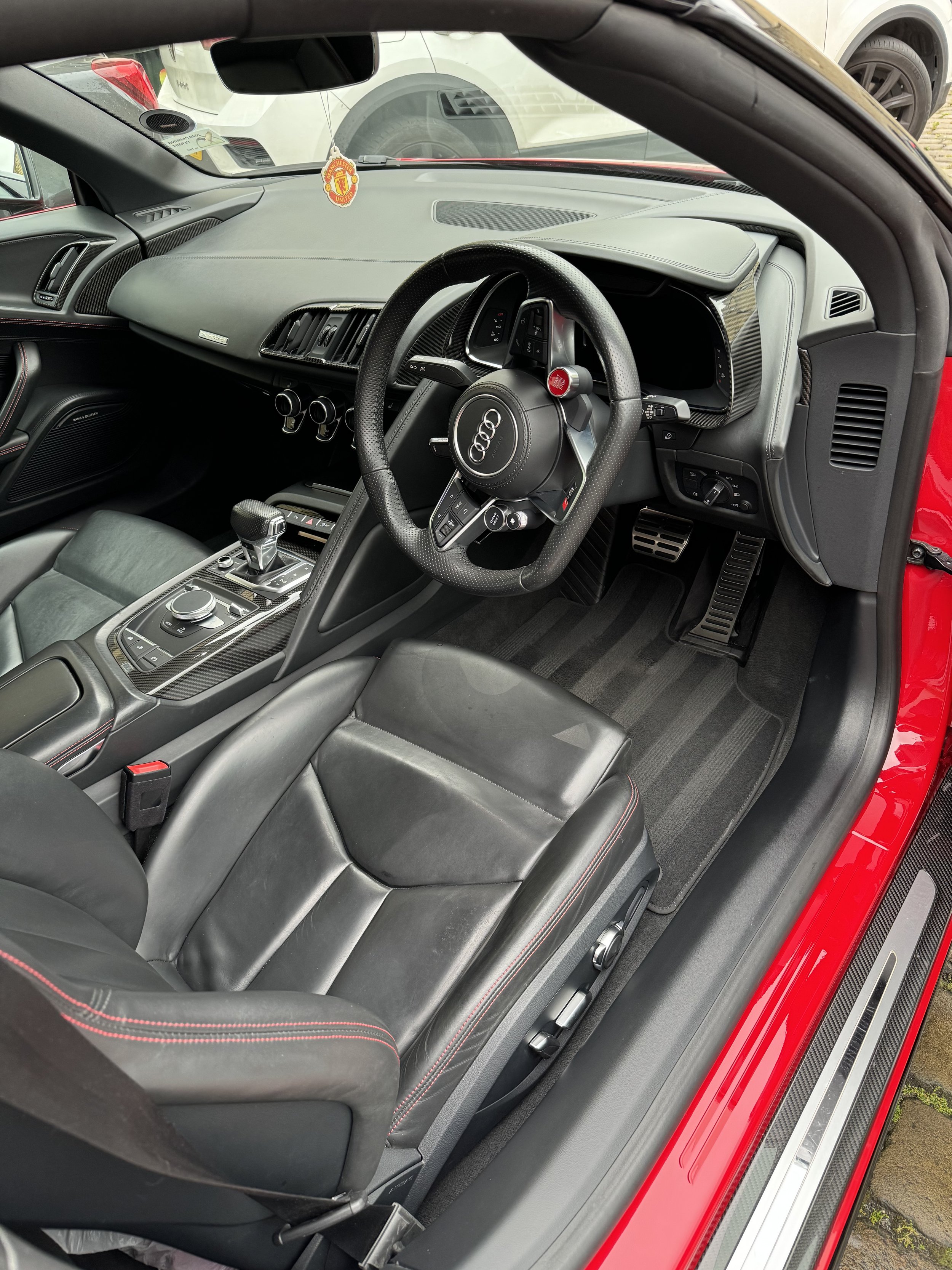 Interior of a red Audi sports car, showing the steering wheel, dashboard, center console, and black leather seats with red stitching.