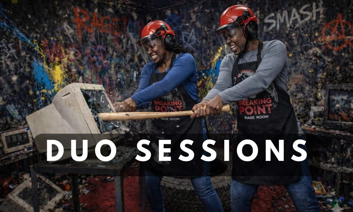 Two smiling people wearing safety gear smash a computer monitor together with baseball bats during a Duo Session at Breaking Point Rage Room