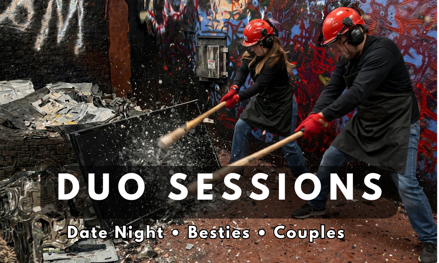Two people wearing red helmets, safety glasses, ear protection, and black aprons smash electronic debris with sledgehammers in a graffiti-covered room. The floor and surroundings are scattered with broken electronics and debris.