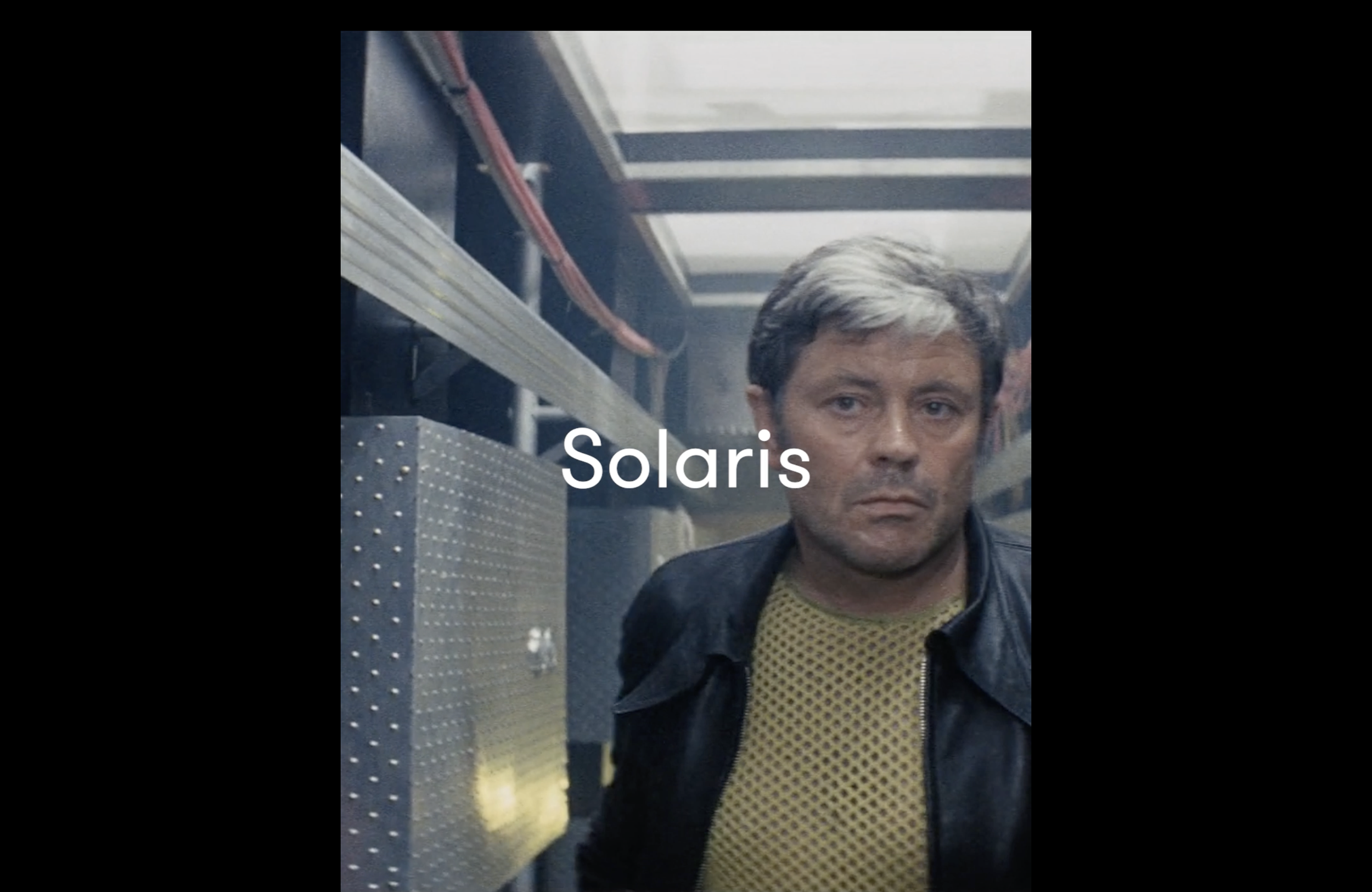 A man with short, slightly disheveled hair and a serious expression, wearing a black leather jacket over a yellow mesh shirt, stands in an industrial setting with metal shelves and equipment in the background. The word 'Solaris' is overlaid in white text.