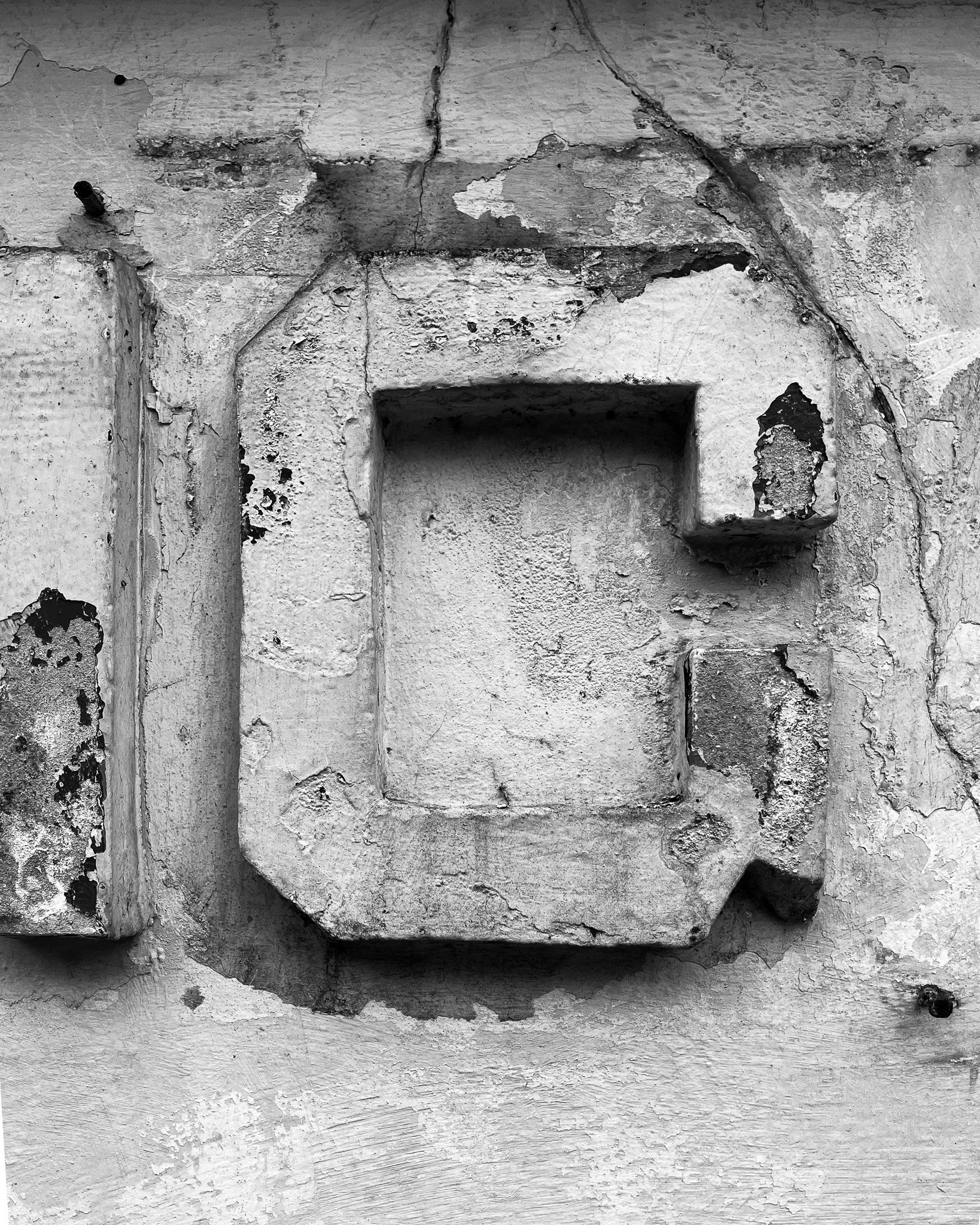 Close-up of a weathered and cracked concrete wall with an embedded rectangular opening and metal rods protruding from the surface.