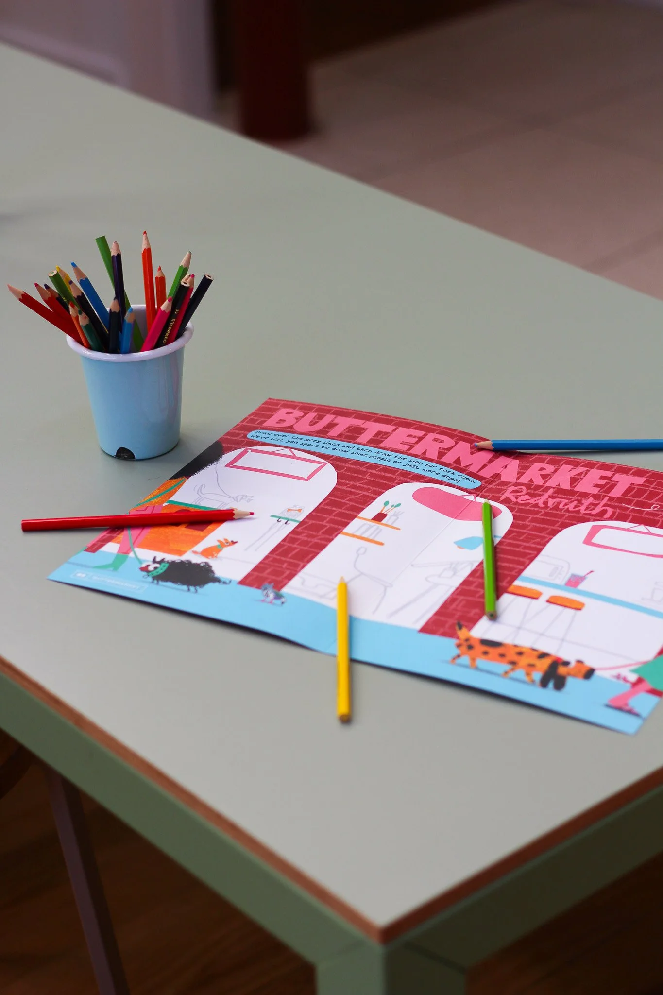 Colorful coloring pages with animal illustrations, several colored pencils, and a cup holding additional colored pencils on a table.