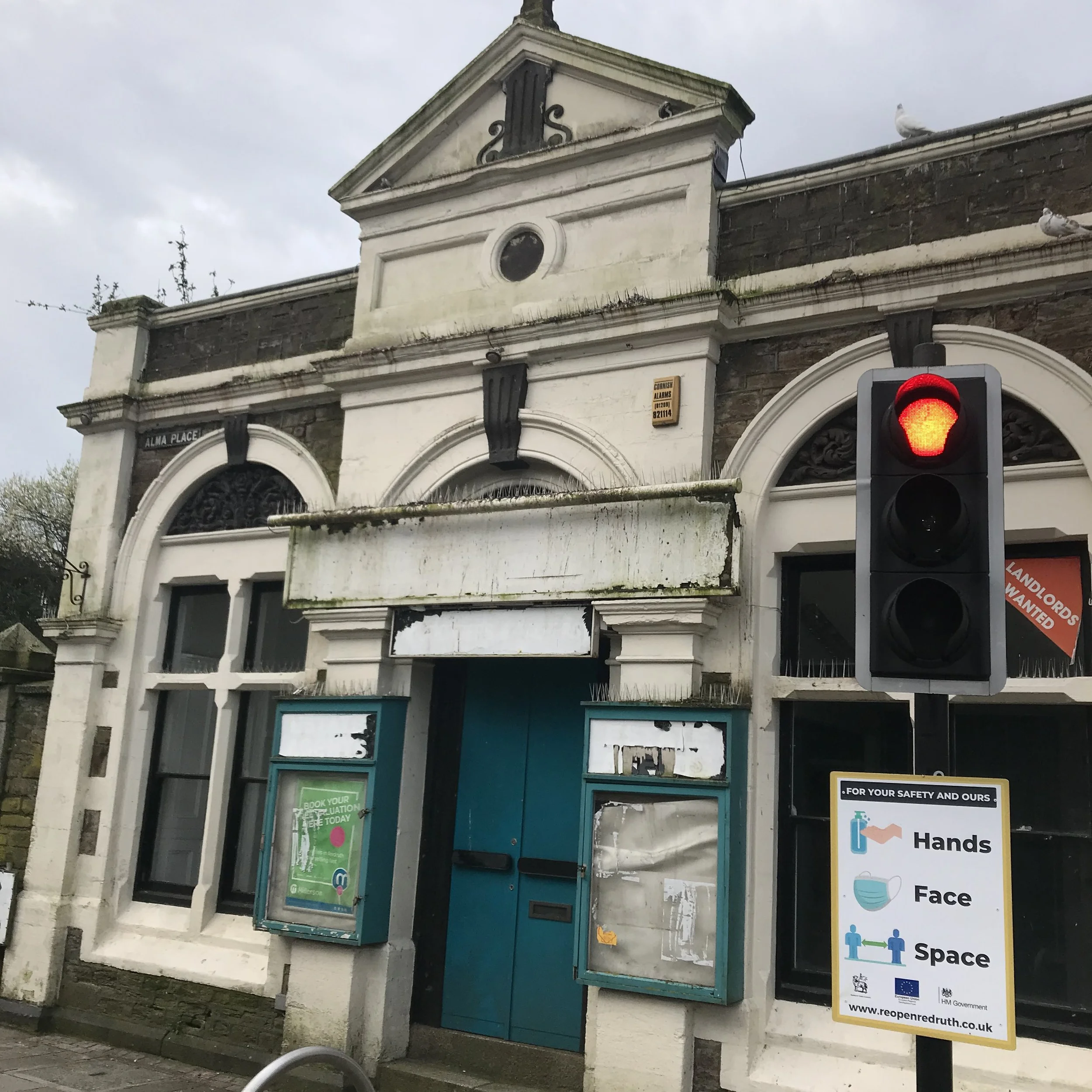 An old, weathered building with a sign for a lost and found office and a red traffic light in front. There are several pigeon birds perched on the building and the traffic light.