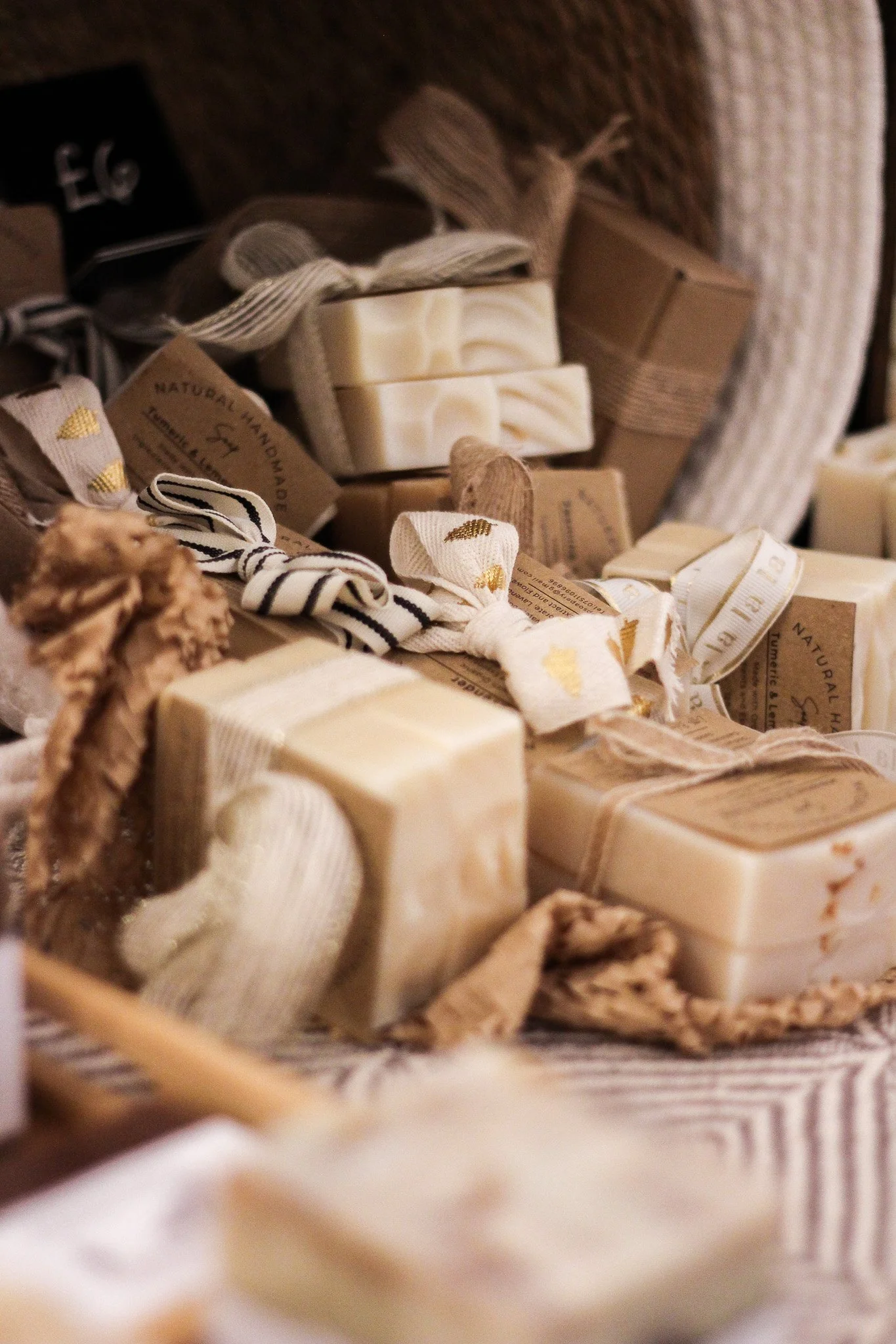 Assorted handmade soap bars, wrapped ribbons, and small gift boxes in neutral tones, arranged in a wicker basket.