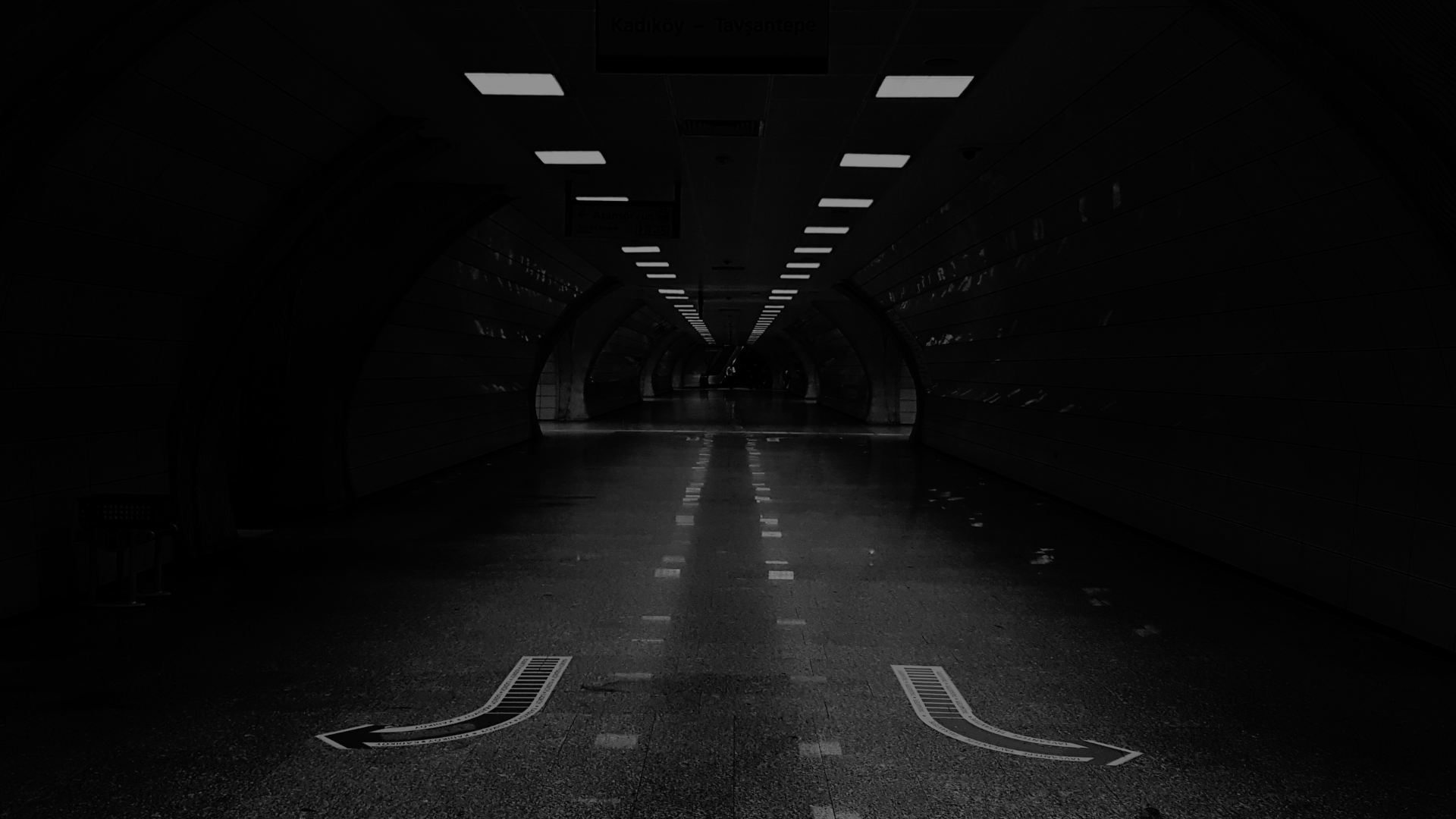 Ein dunkler, leerer Tunnel mit künstlicher Beleuchtung und Wegweisung auf dem Boden.