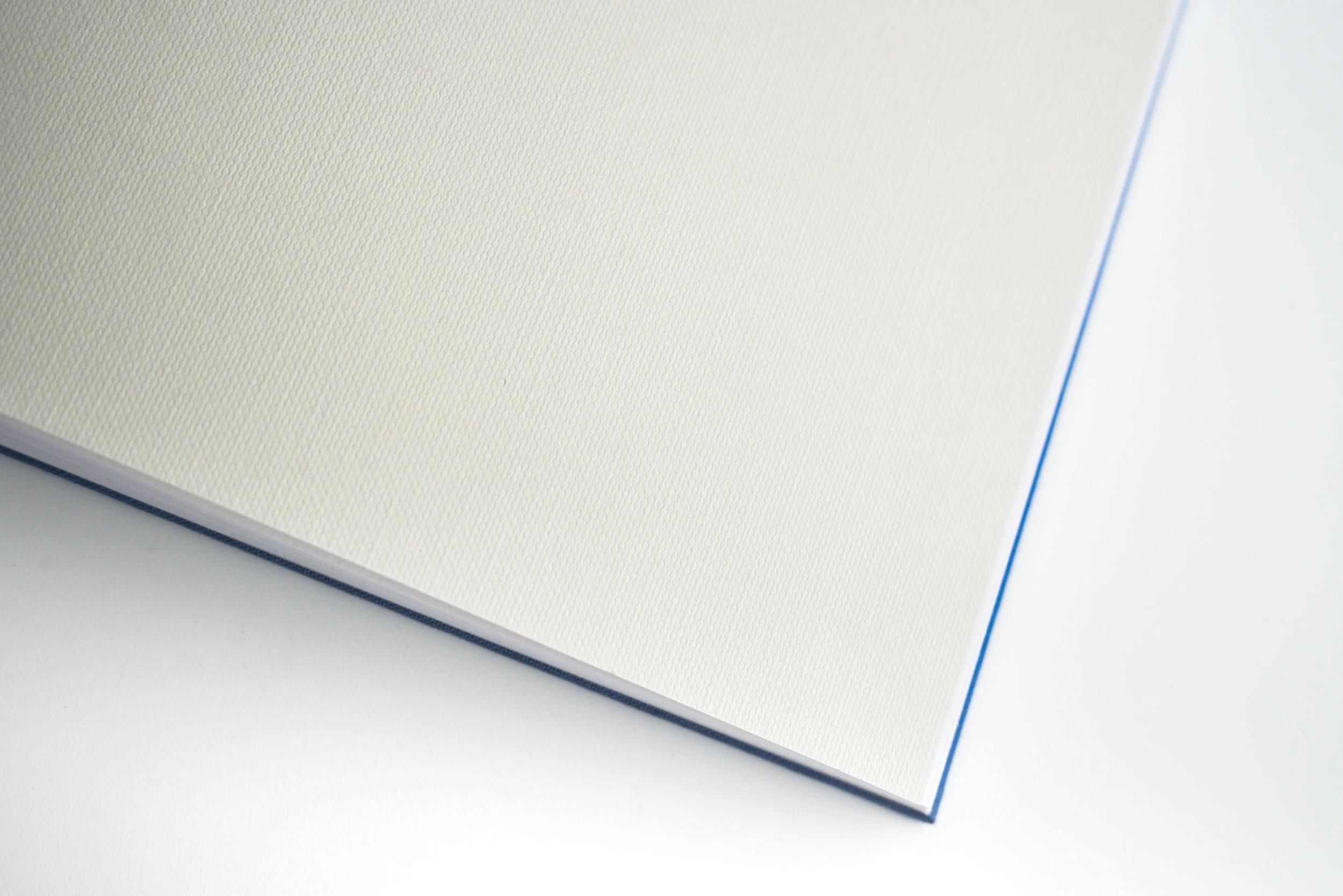 Close-up image of a corner of a white notebook or journal with textured pages, blue edges, and a light blue line on the right side.