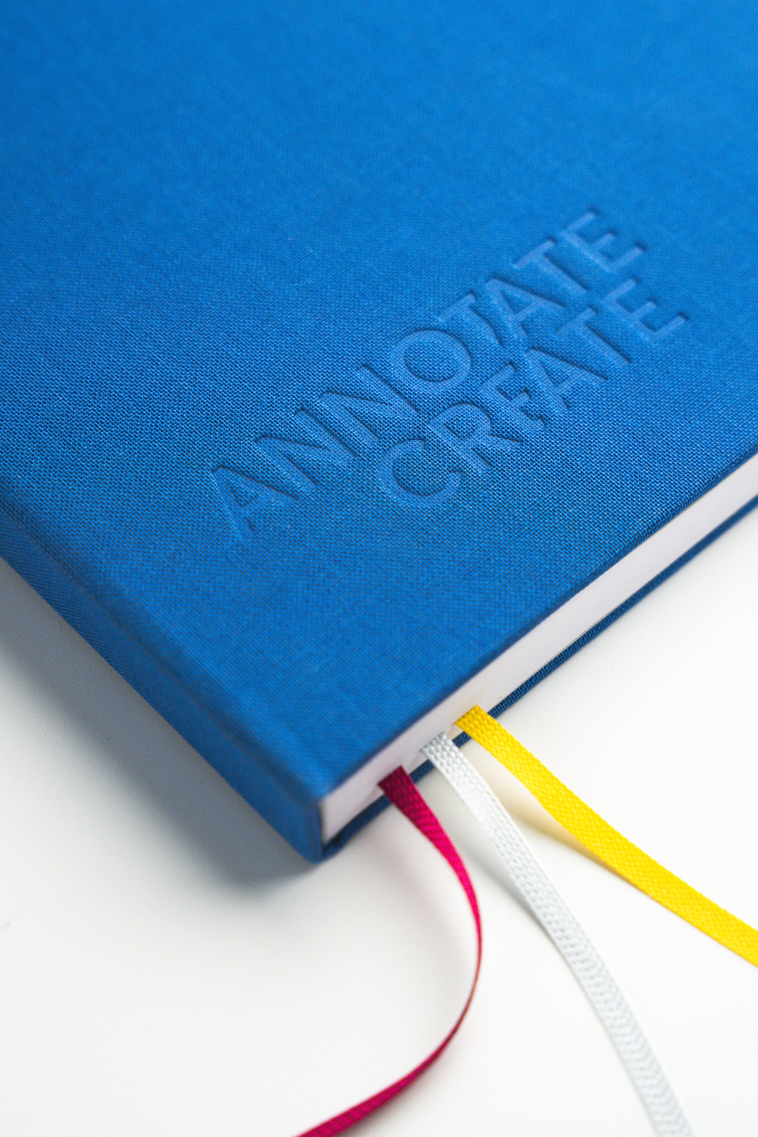 Close-up of a blue notebook with the embossed text 'AN Notebook' and colorful ribbon bookmarks