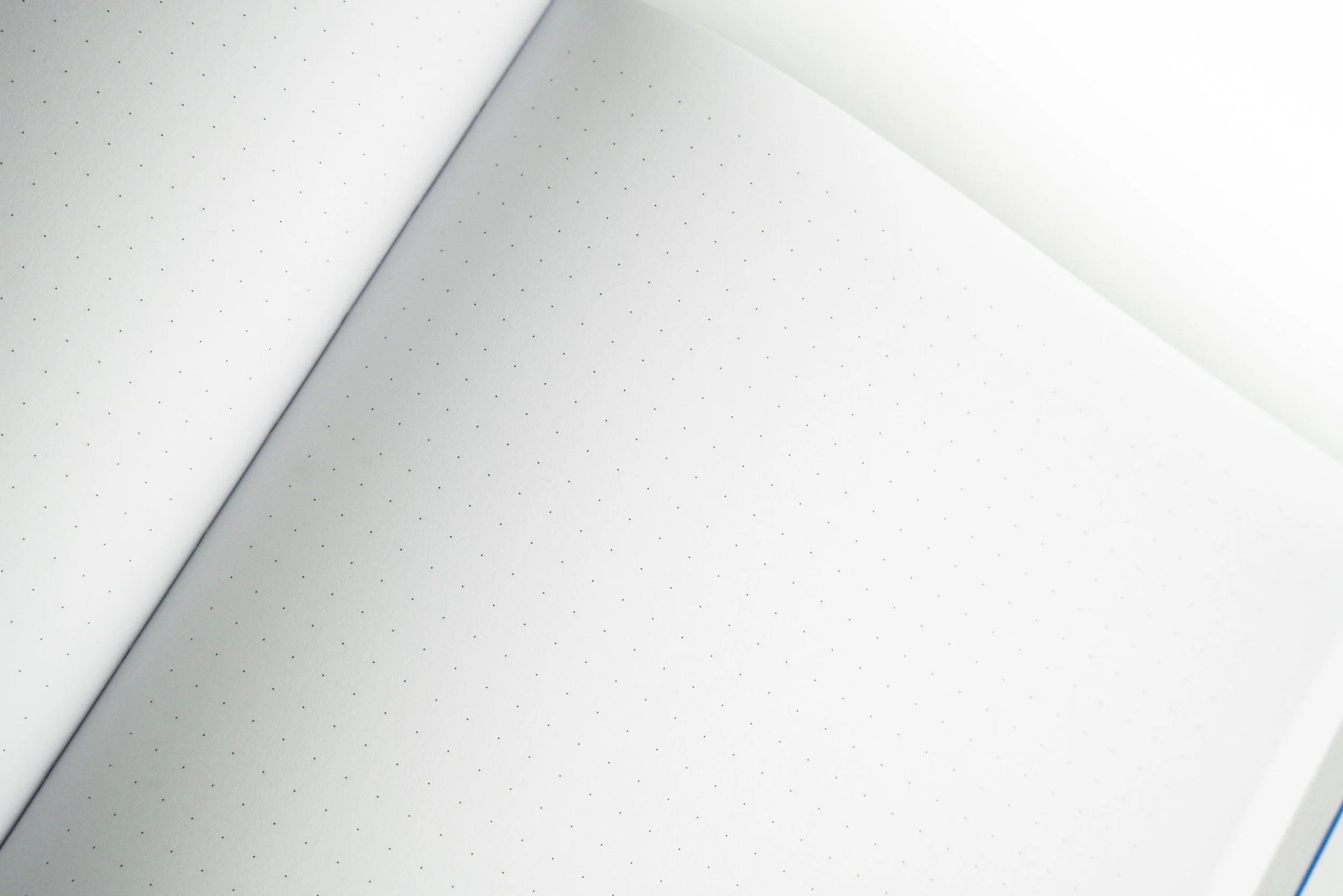 Close-up of white dotted notebook pages with one page turned over, revealing the dotted pattern.