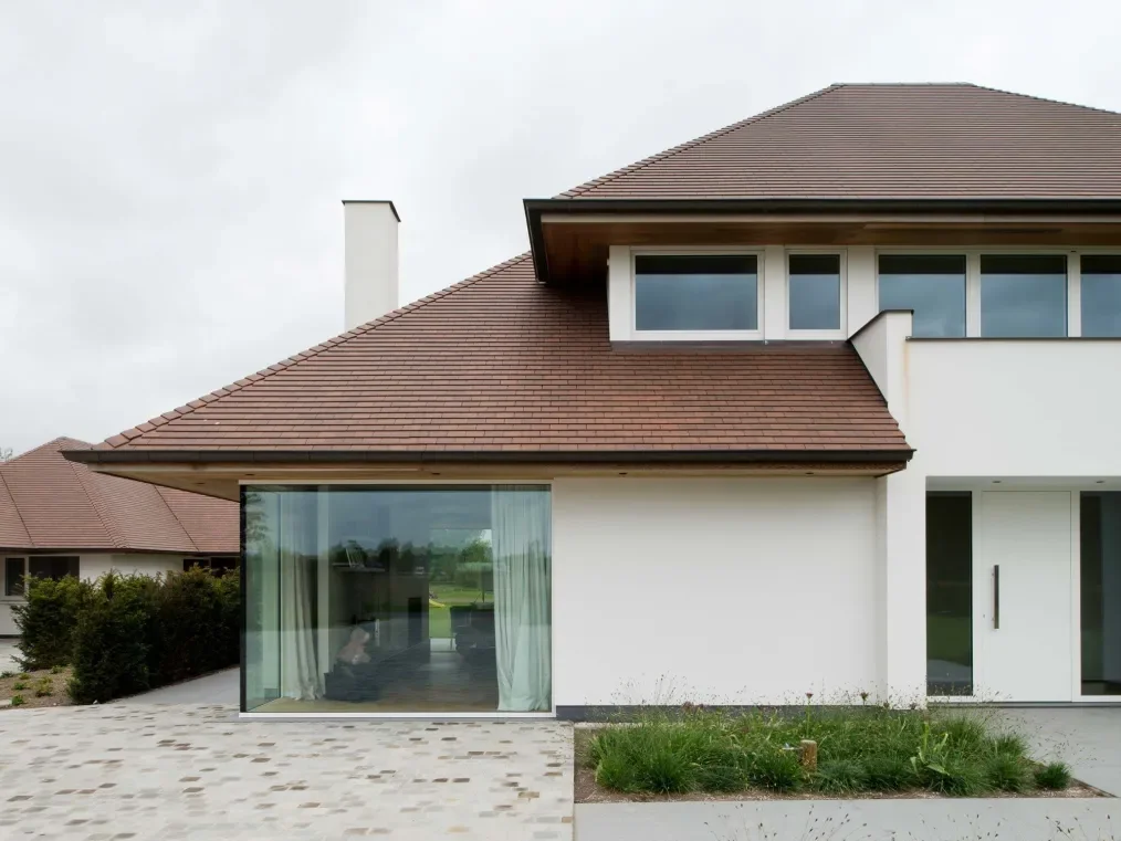 Modern house with white walls, large windows, brown roof, and a small garden in front.