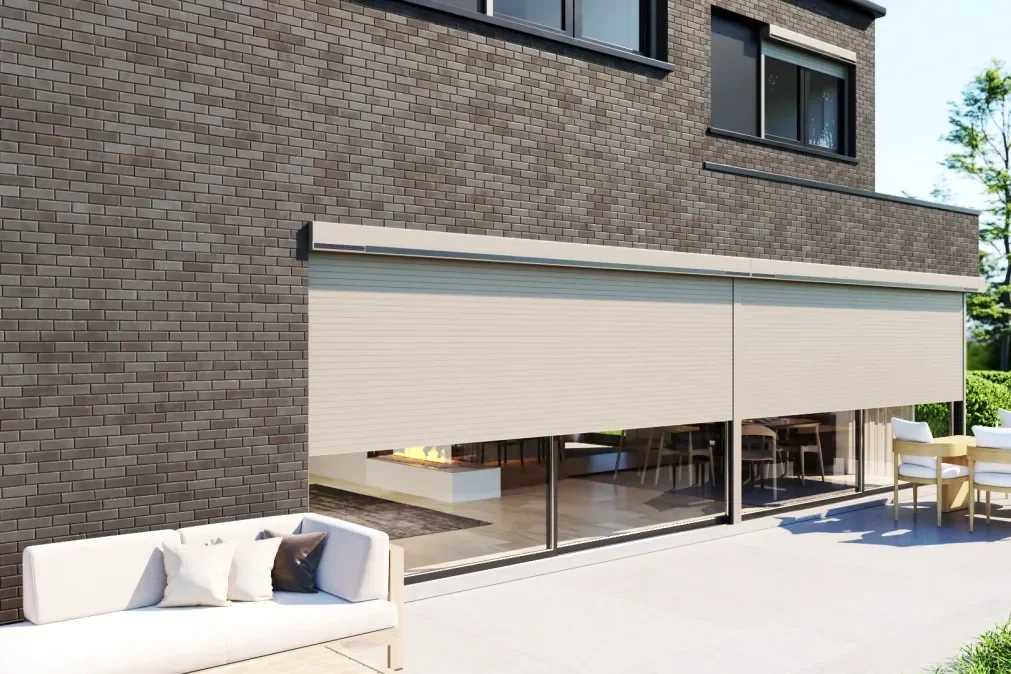 Modern house with brown brick exterior, large glass sliding doors, outdoor patio with white cushioned sofa, and dining table with chairs