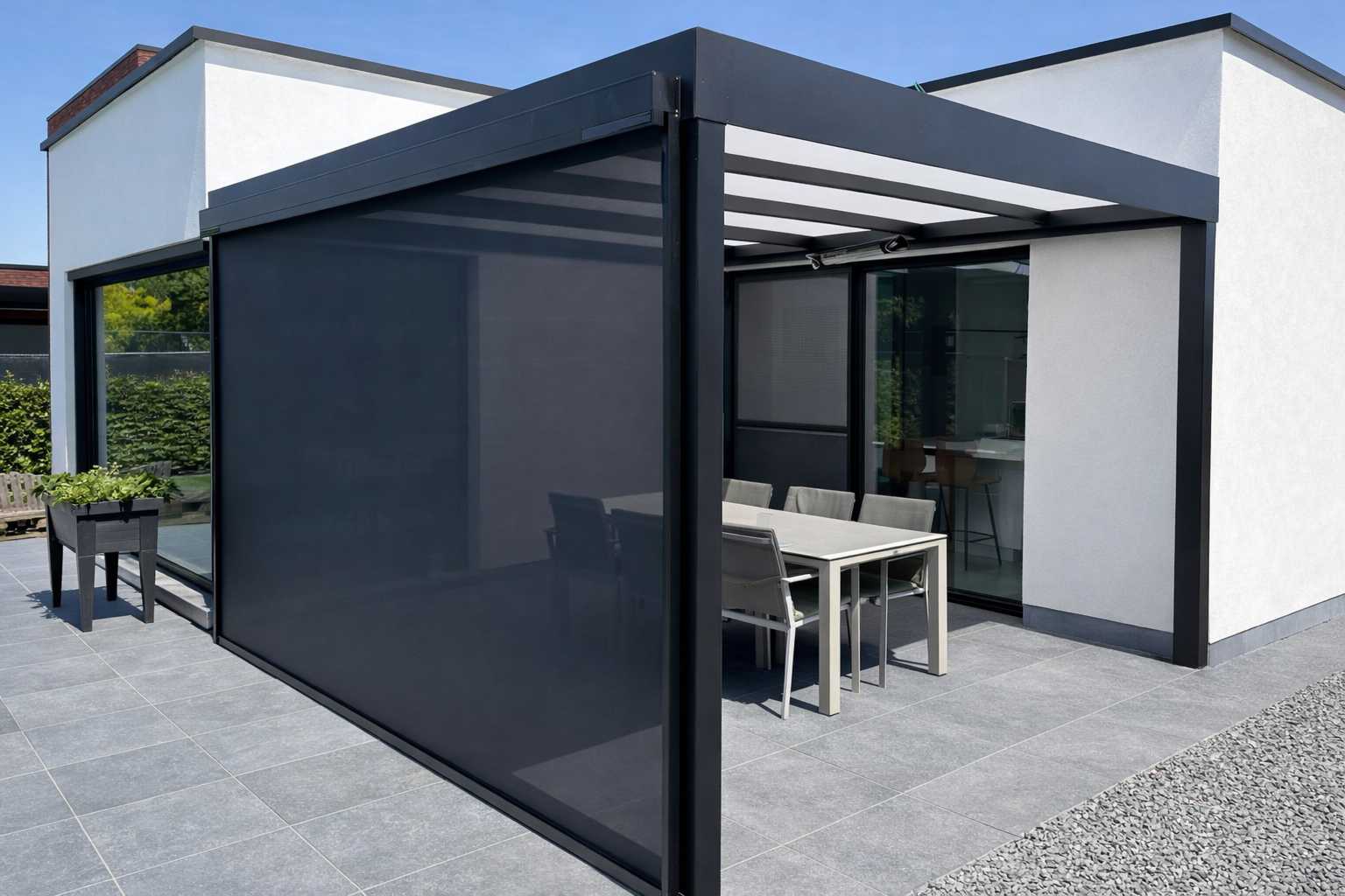Modern outdoor patio with a dining table and chairs, enclosed by black metal and dark screen panels, attached to a white building with large glass sliding doors, on a sunny day.