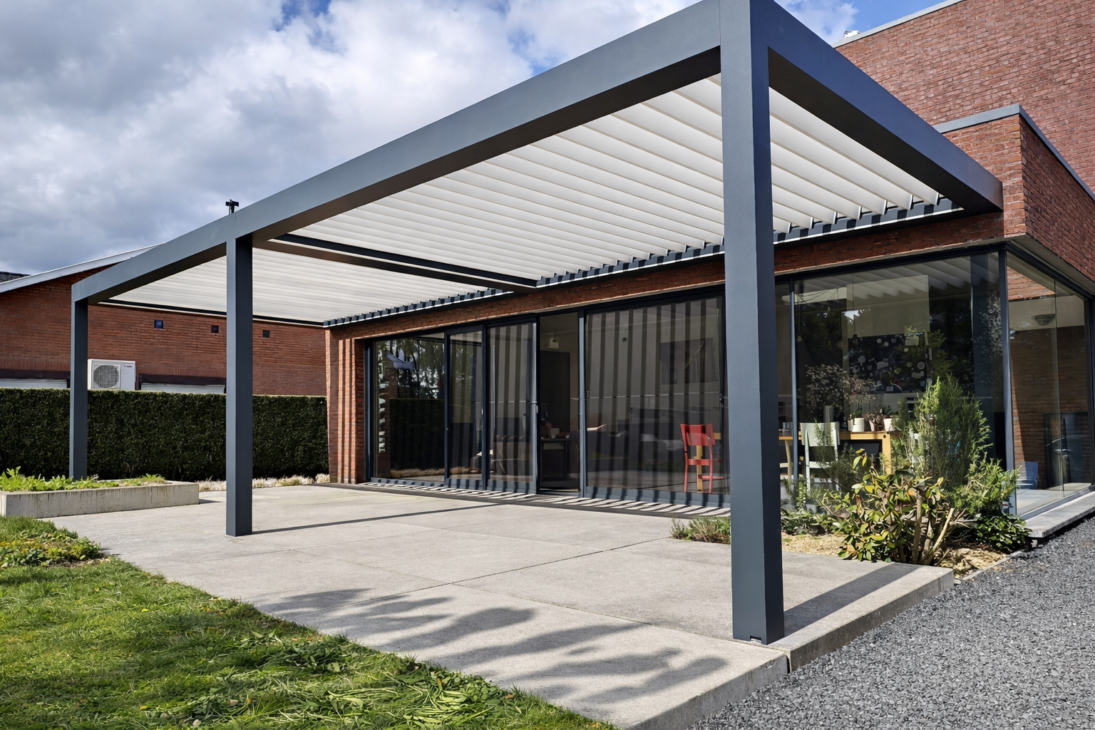 Modern house with a covered patio area featuring a metal frame and white retractable awning, glass sliding doors, a small garden, and a concrete pathway.