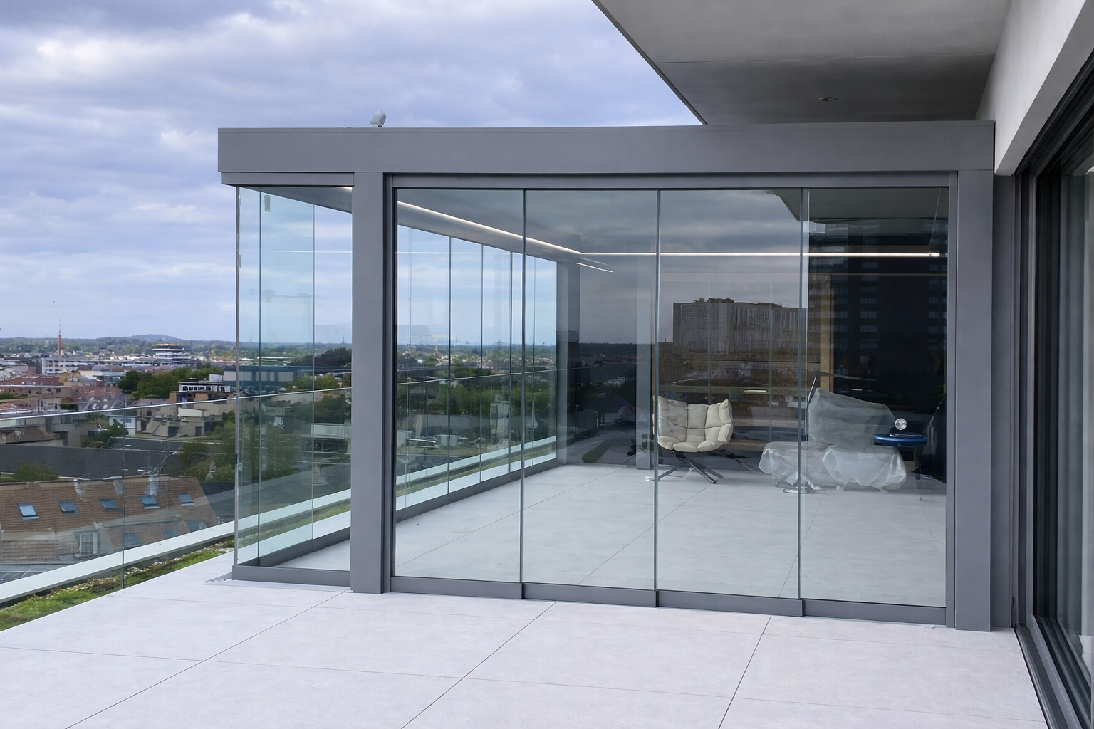 Modern balcony with glass walls and minimalistic furniture, overlooking an urban landscape with buildings and trees under a cloudy sky.
