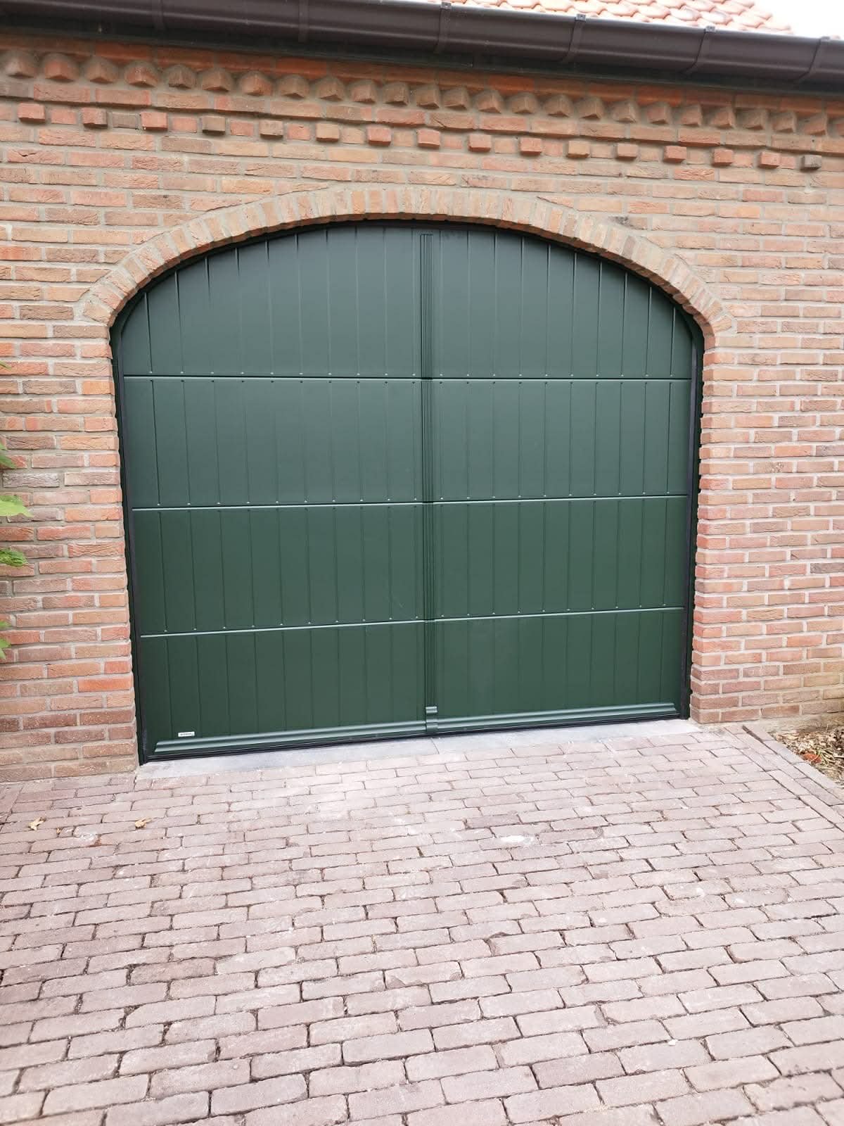 Green garage door with brick framing and brick driveway in front.