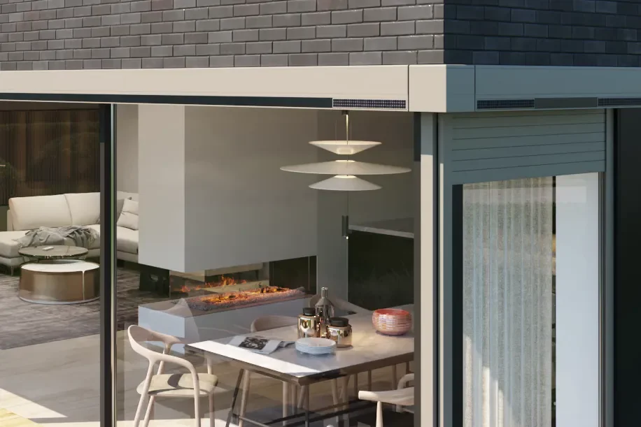 Modern dining area with a fireplace, table set with dishes and a chandelier, adjacent to a living room with a sofa, seen through large glass windows.