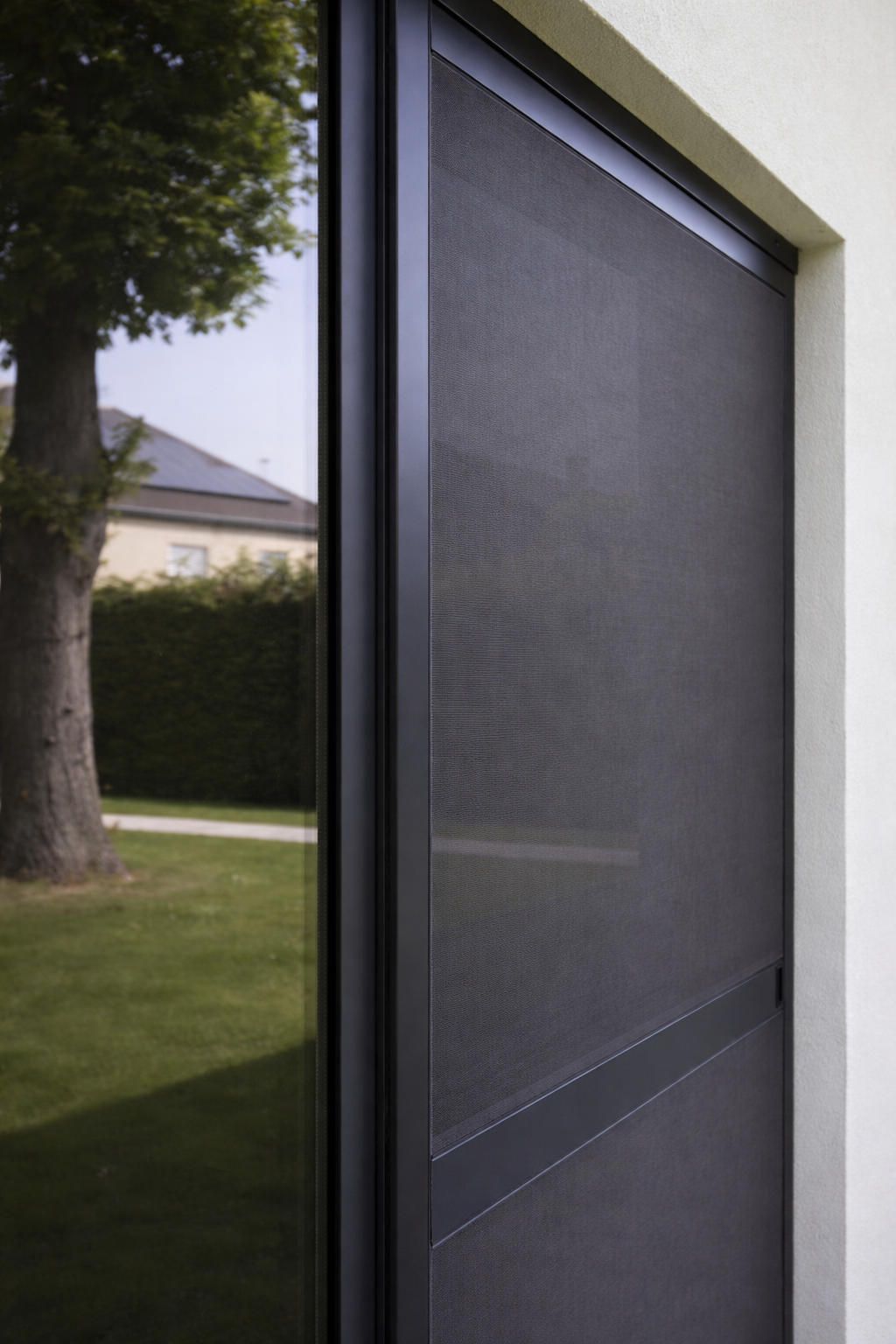 Close-up of a window with a black screen or mesh, reflecting greenery and a house outside.
