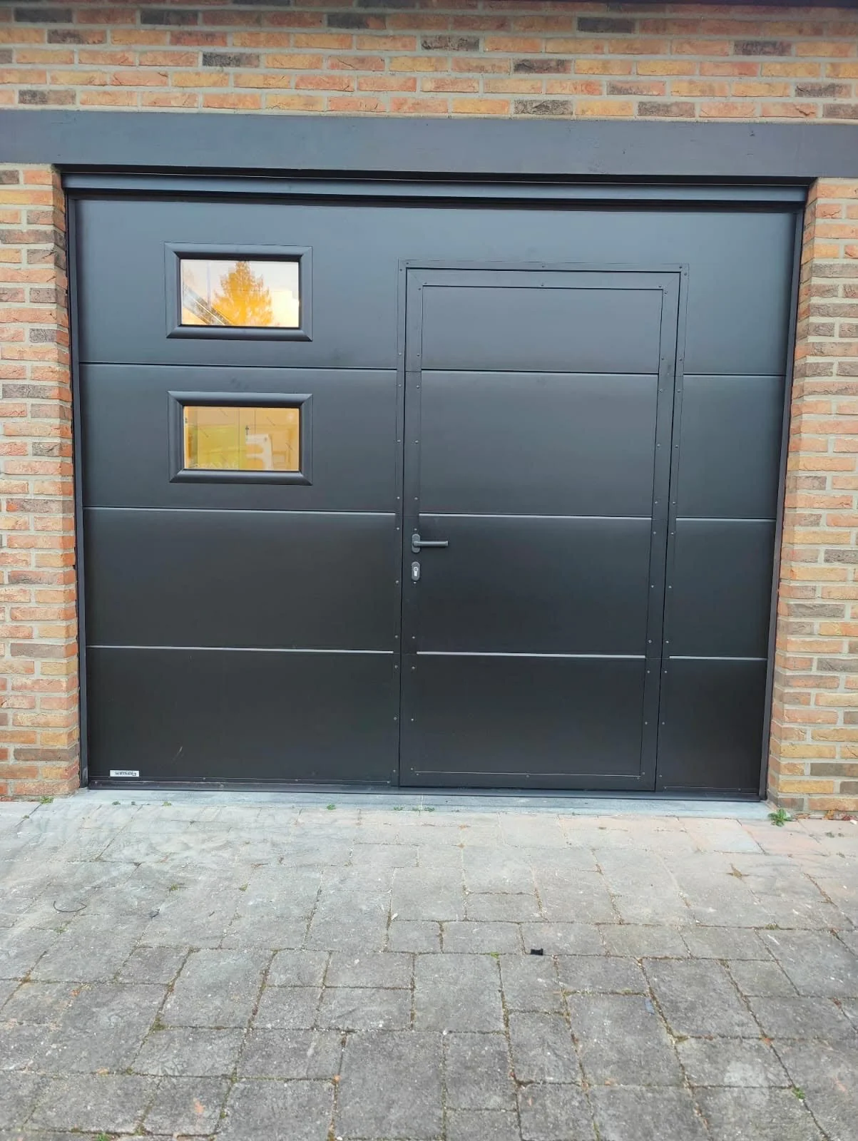 Black garage door with two small windows set in a brick wall.