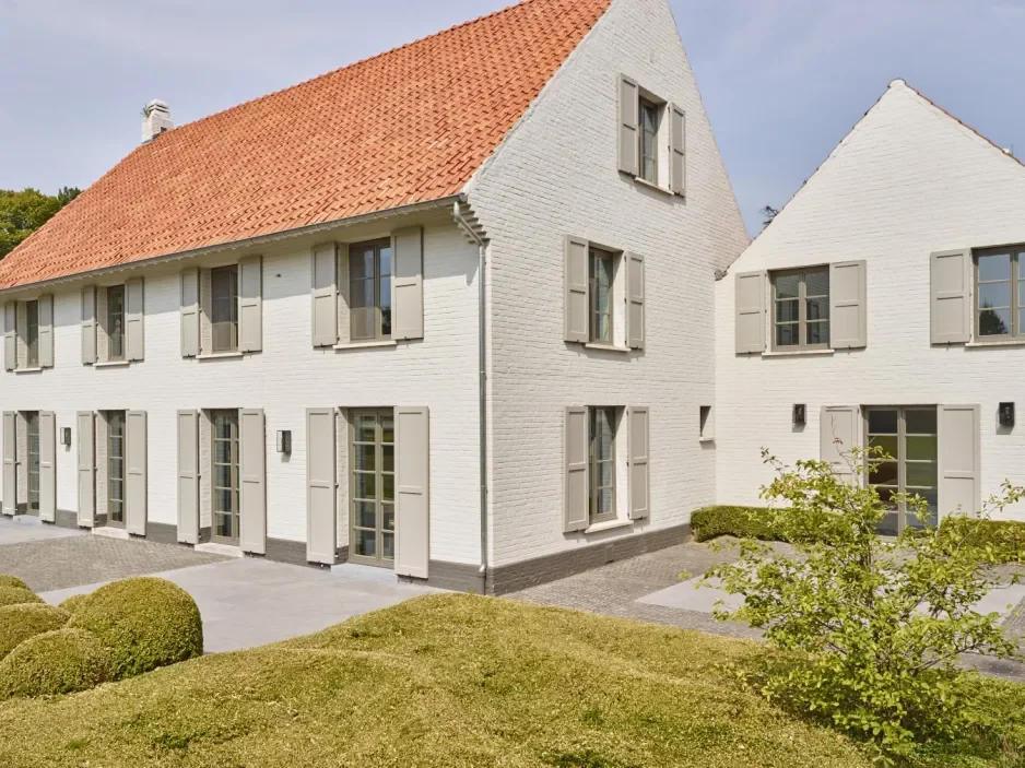 White brick houses with beige shutters and red tile roofs, surrounded by a lawn and small bushes.