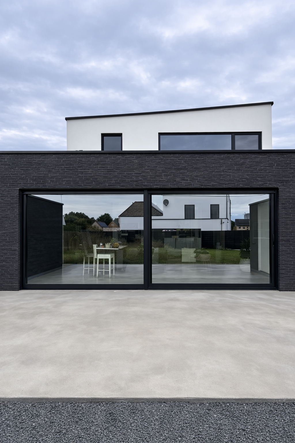 Modern house with large glass sliding doors, black brick exterior, and a white flat-roofed upper level, under a cloudy sky.