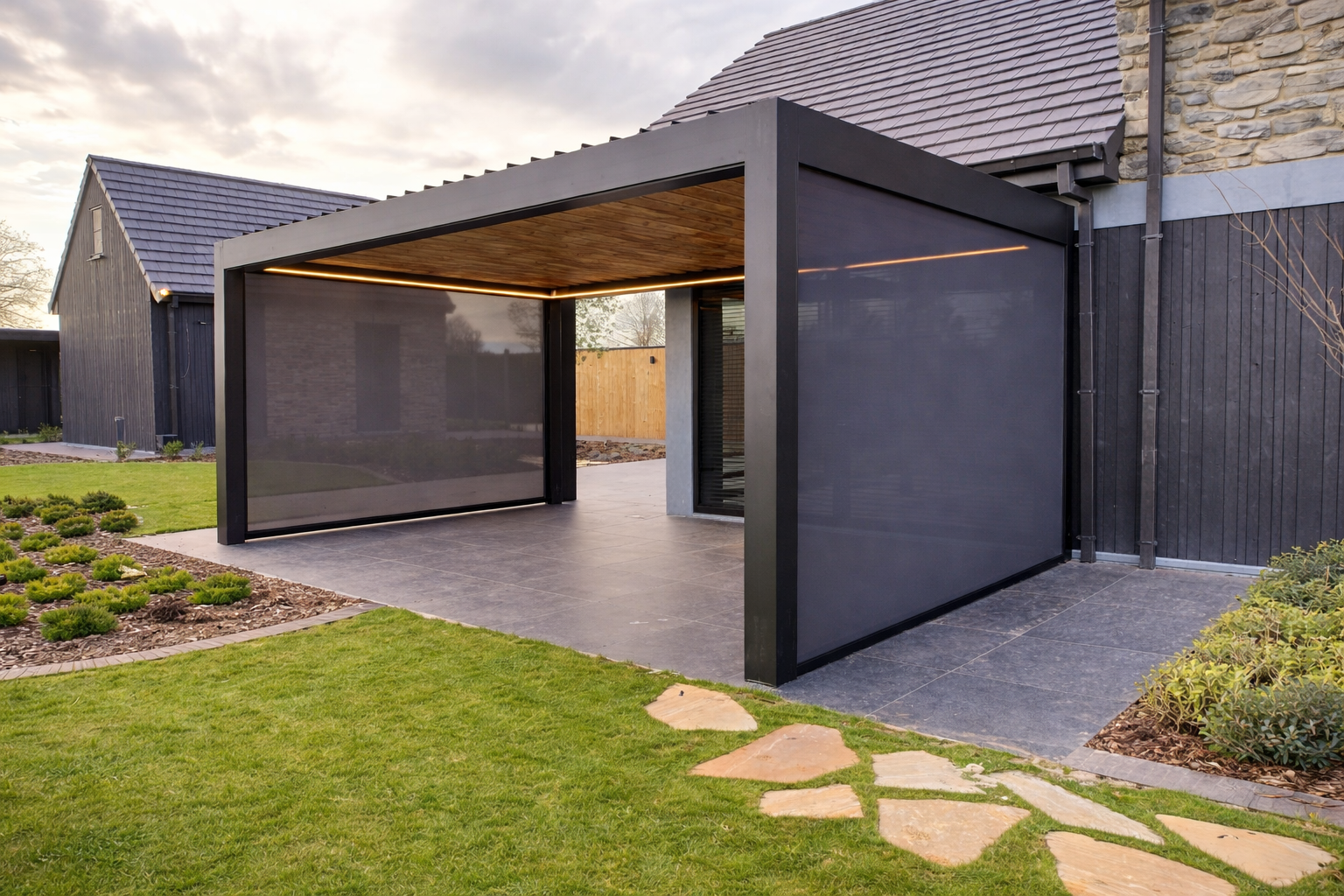Modern backyard patio with a black metal and wood pergola, surrounded by a green lawn, stepping stones, and house with dark siding.
