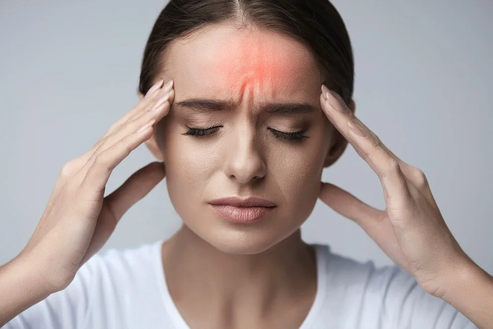 A woman holding her head with a pained expression, indicating a headache or migraine, with redness on her forehead.