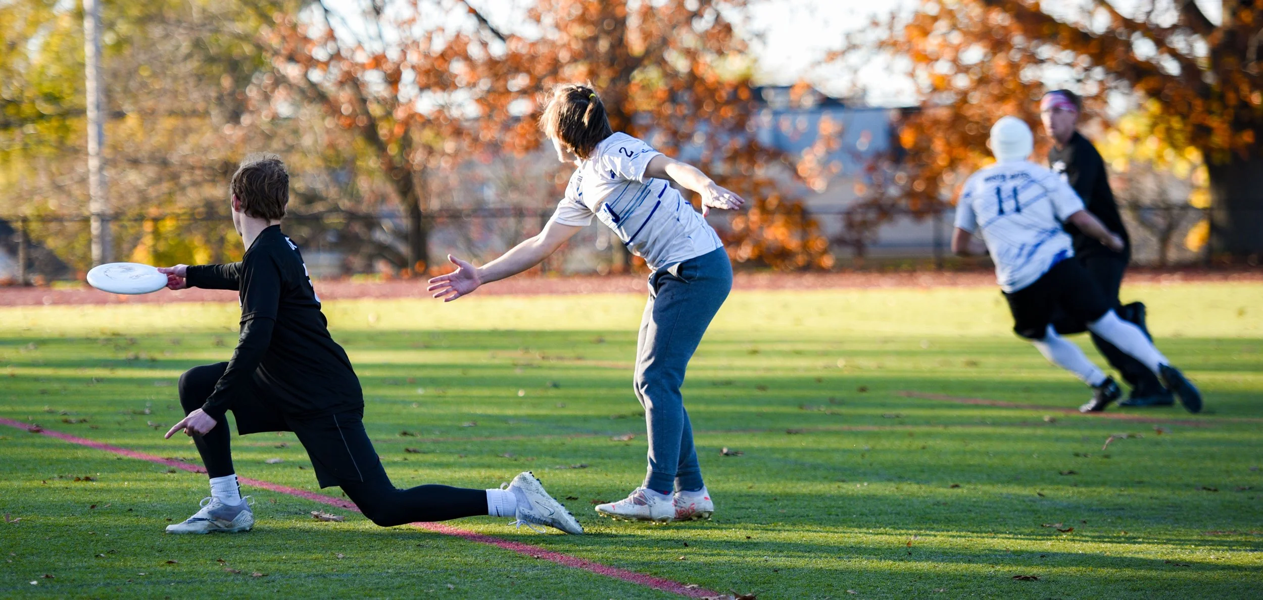 Children playing ultimate frisbee on a grassy field during autumn, with trees with orange leaves in the background.