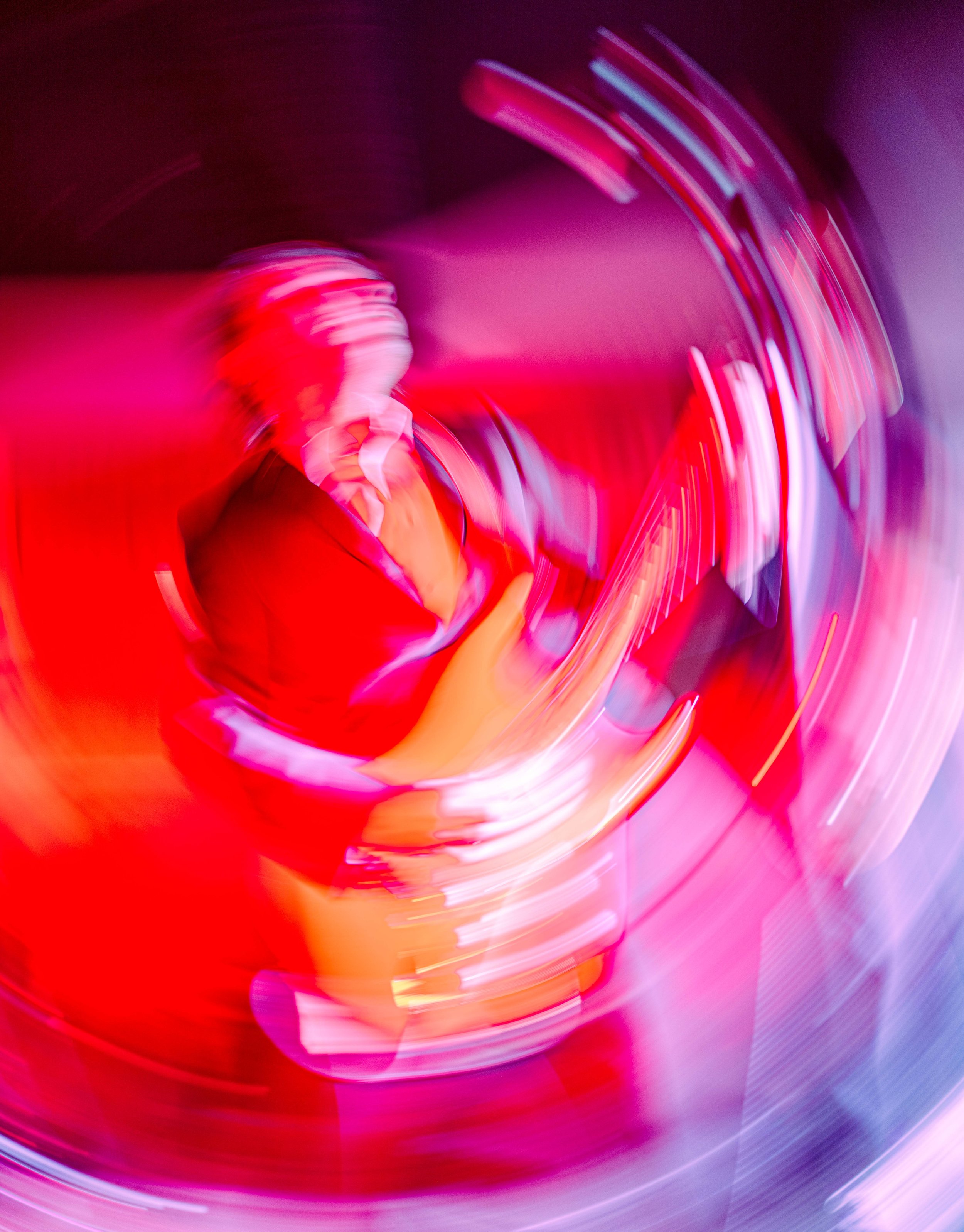 A person with short hair, wearing glasses and a red shirt, captured in a whirl of colorful lights during motion blur photography.