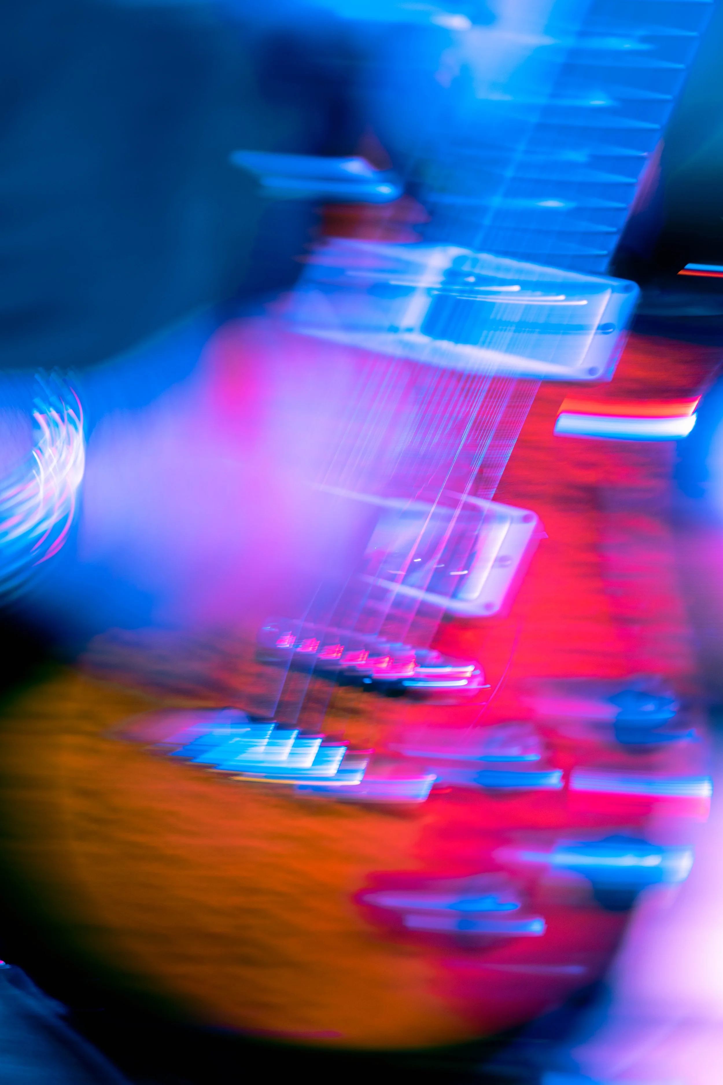 An electric guitar with a colorful, vibrantly lit background, featuring shades of blue, pink, and red, with a blurred and abstract appearance.