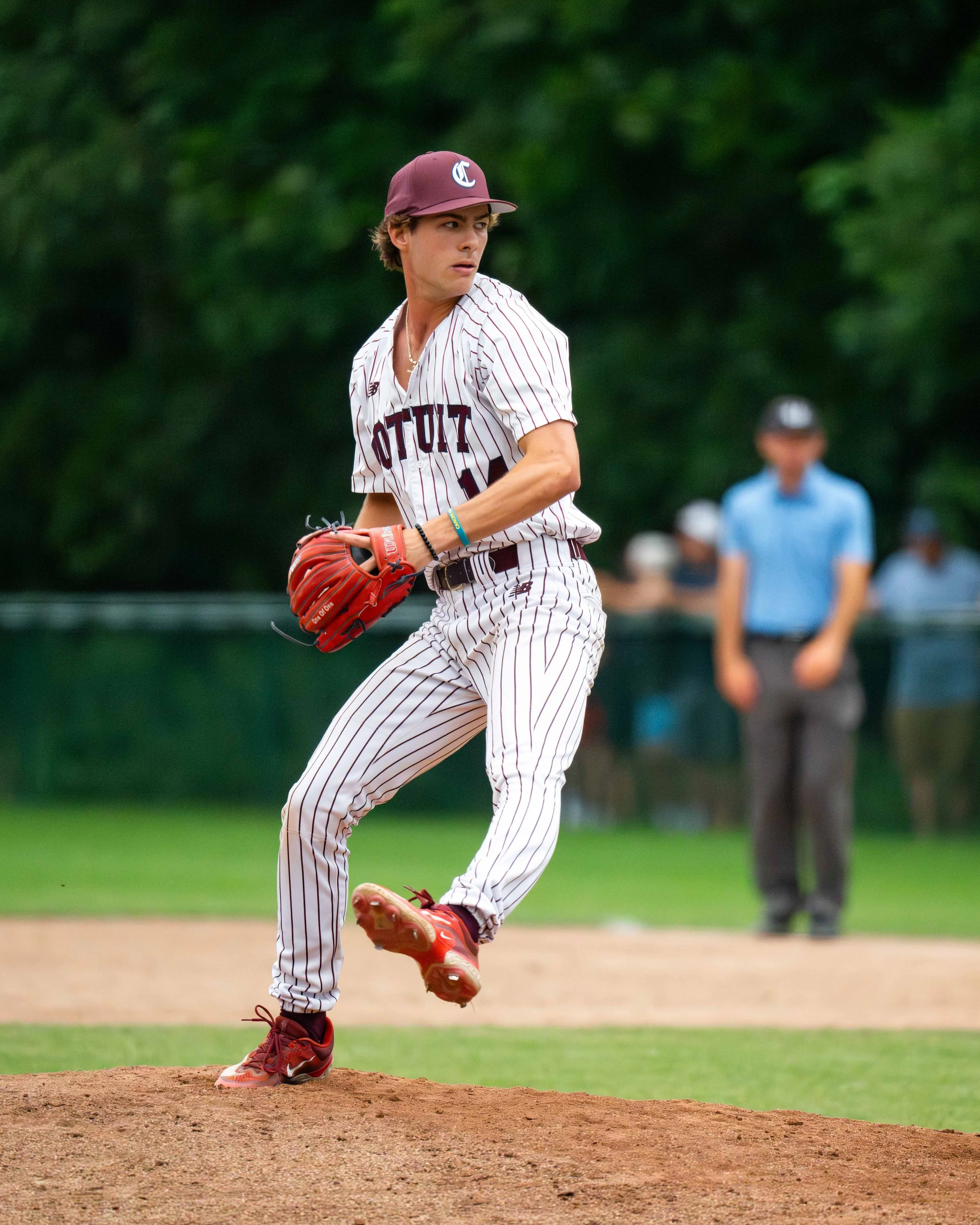 A baseball player in a striped uniform and maroon cap, holding a red glove, standing on a pitcher's mound during a game.