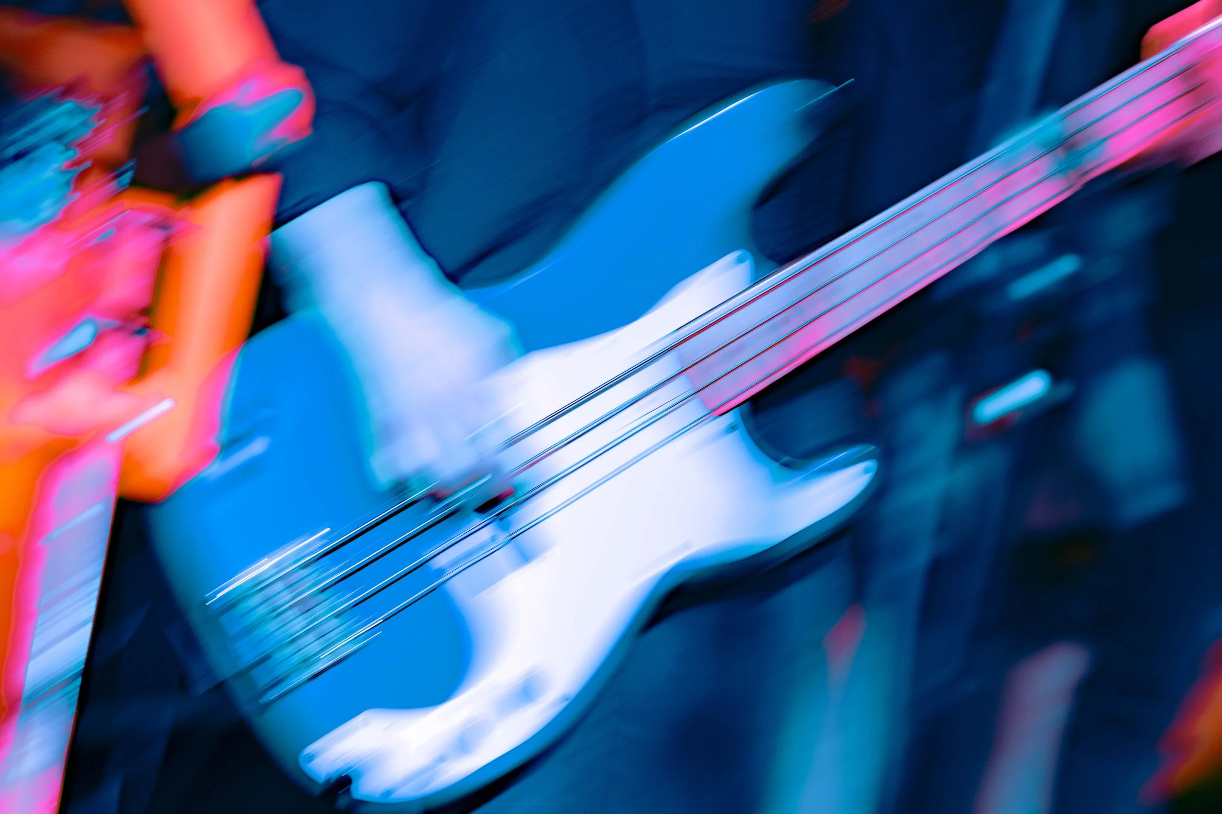 Blurred close-up of an electric guitar with a white pickguard and black body, displaying neon pink and blue lighting effects.