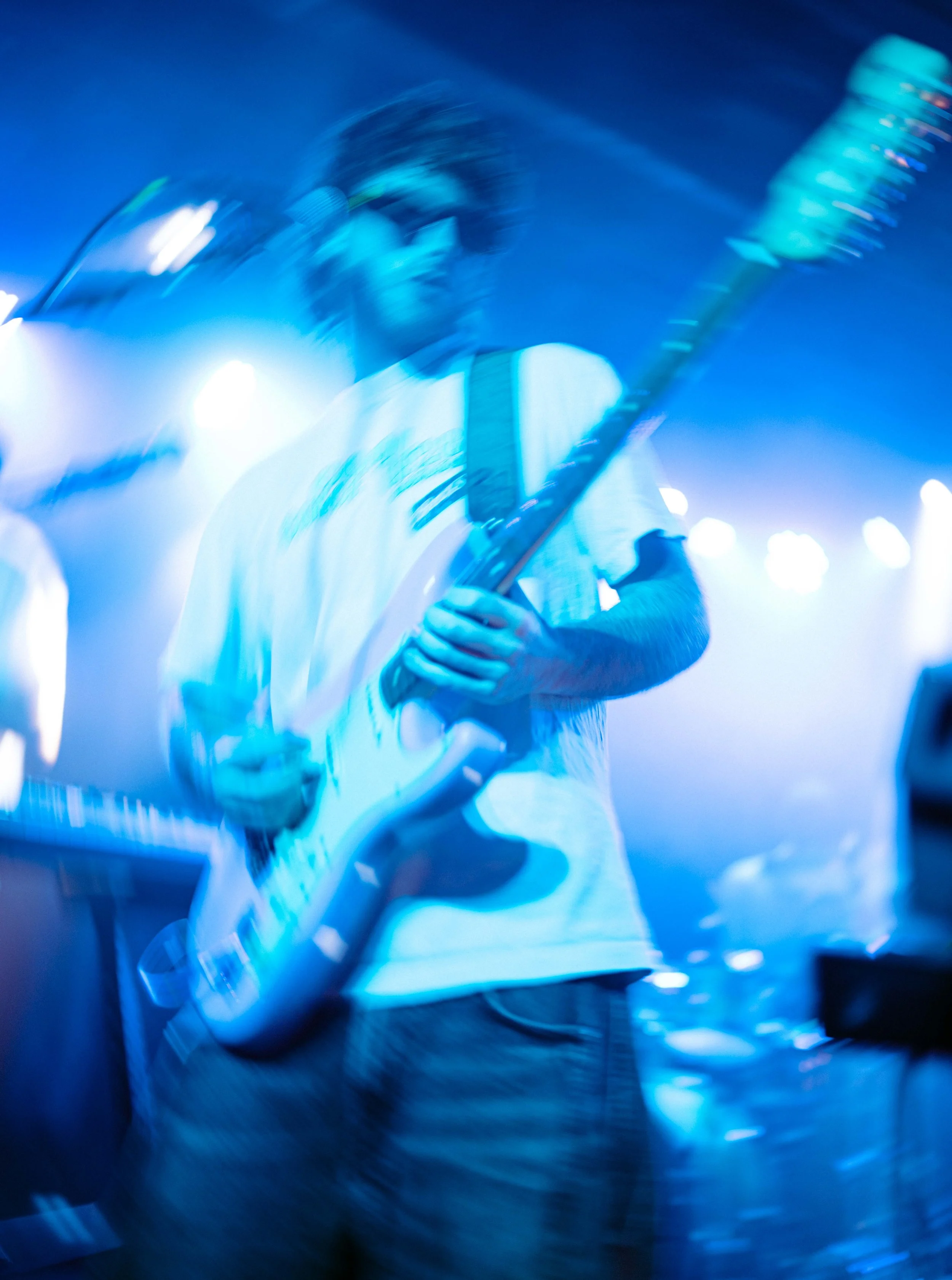 Blurry image of a man playing an electric guitar on stage with blue lighting.