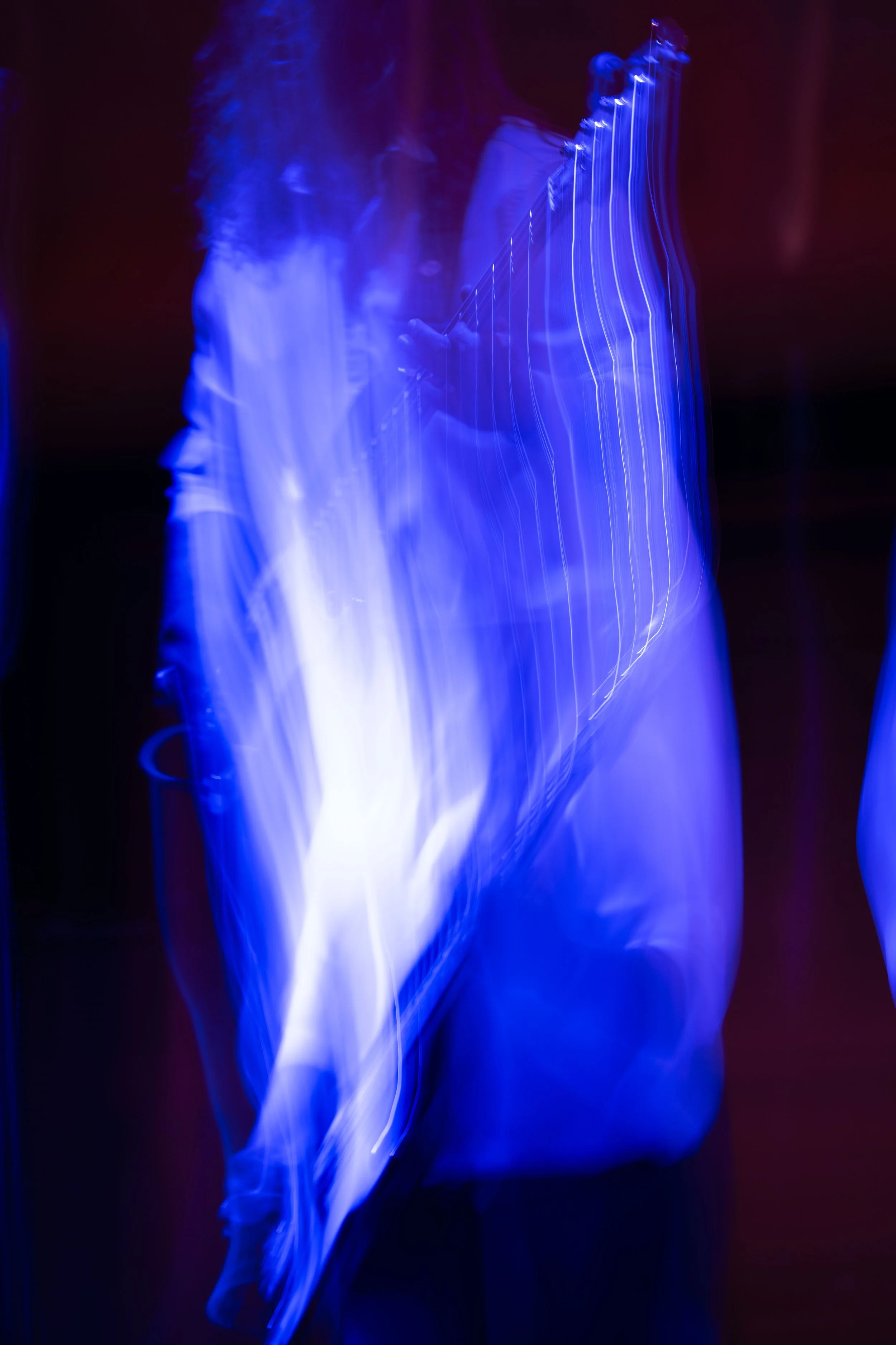 A person playing an electric guitar, captured with long exposure creating motion blur and streaks of blue and white light.