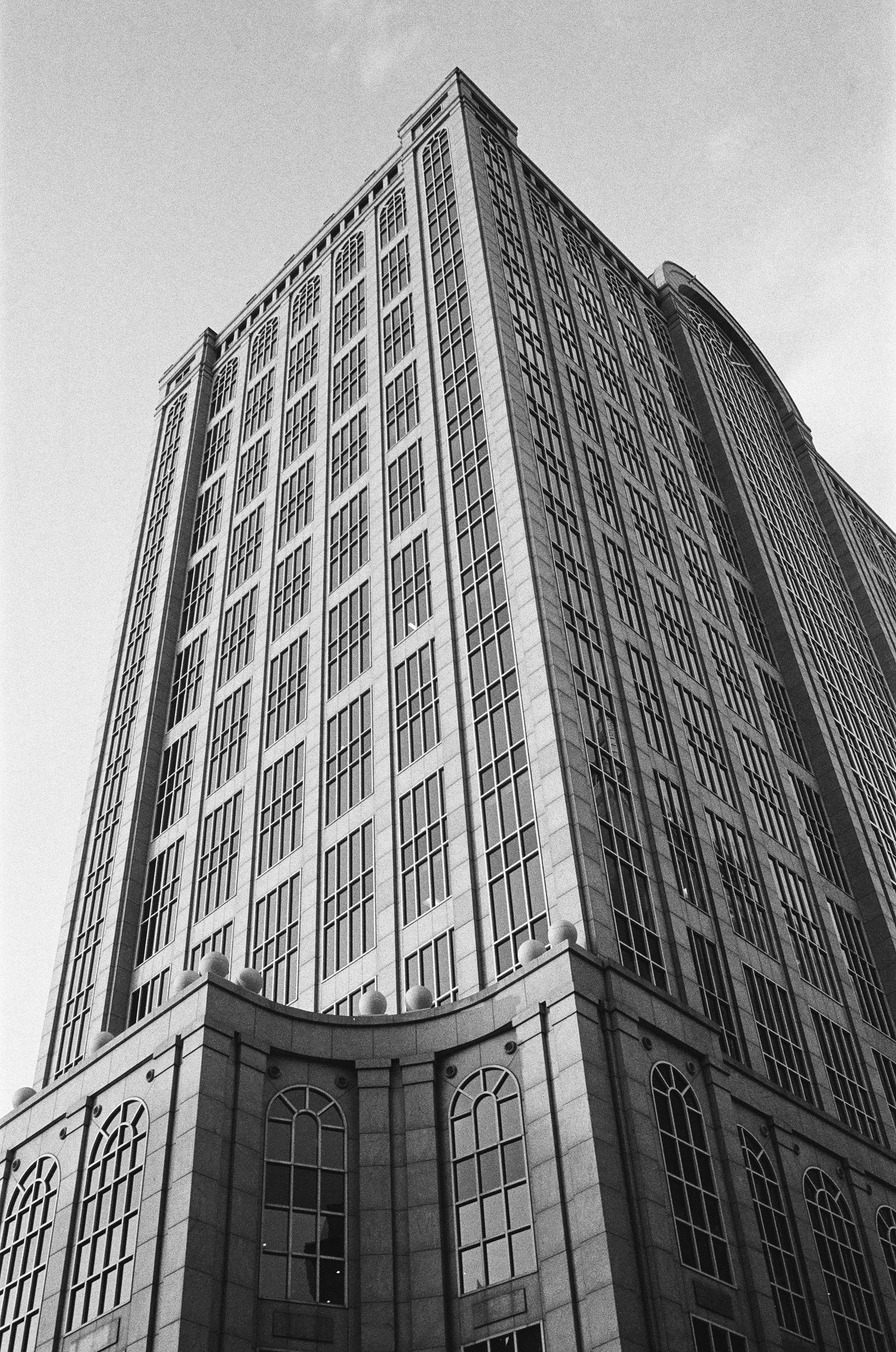 A tall, modern building with many windows, looking up from the street angle, in black and white.