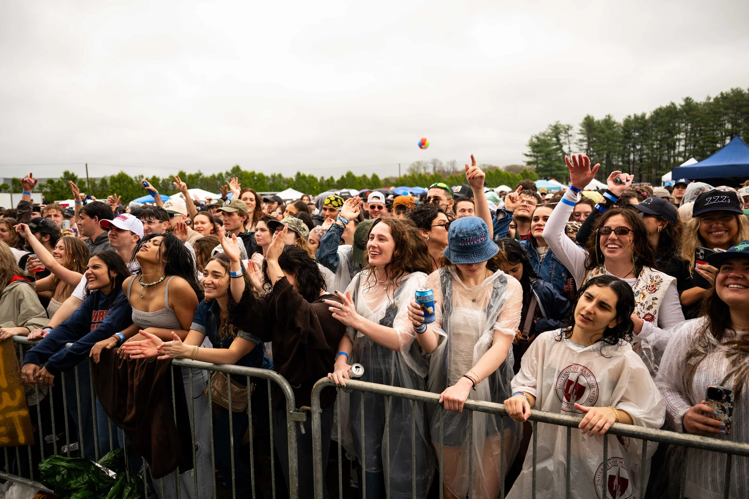 Crowd of young people enjoying outdoor concert, some dancing and smiling, with tents and trees in the background on a cloudy day.