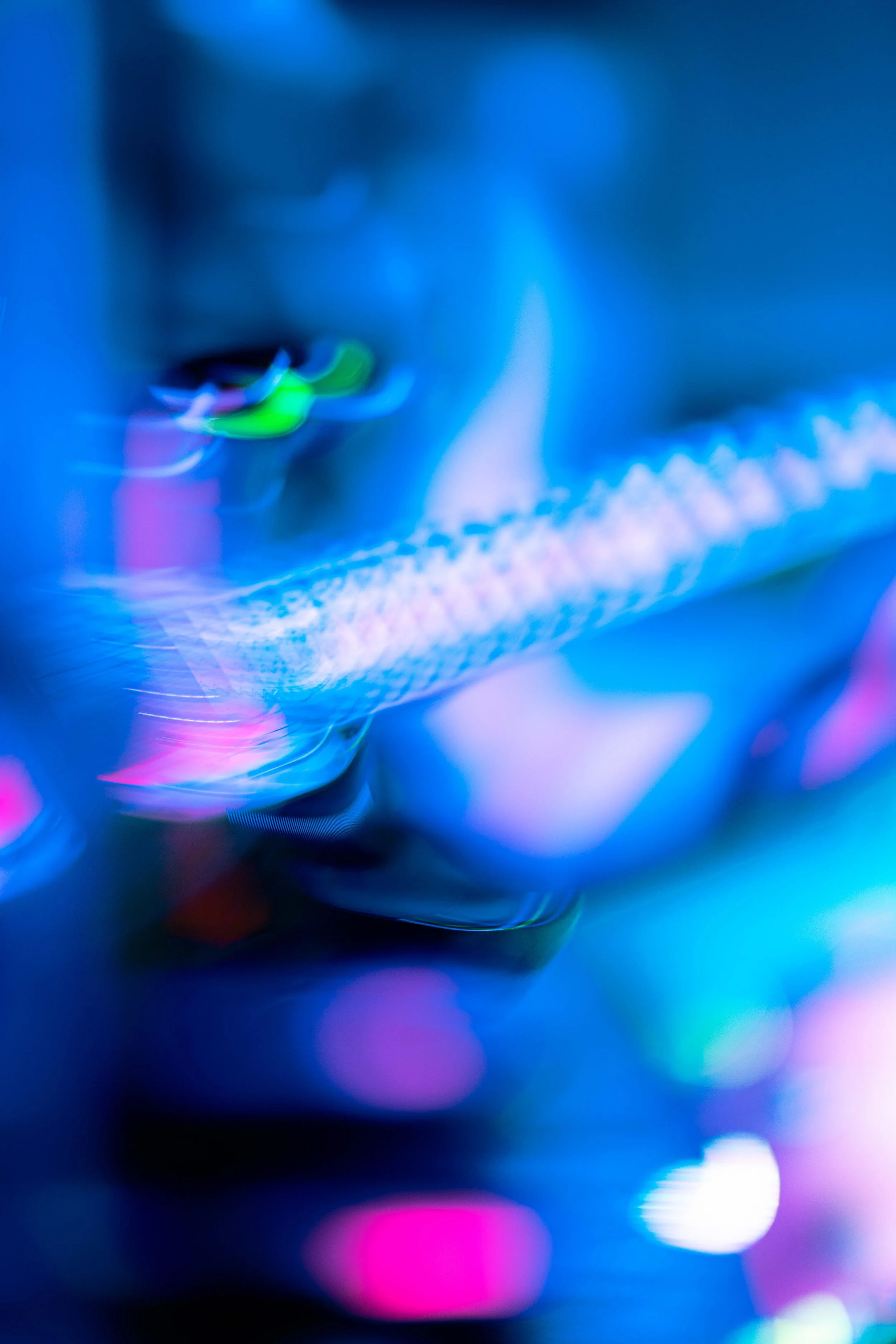 Close-up of colorful, abstract neon lights with a focus on a glowing strip and blurred background in blue, pink, and purple hues.