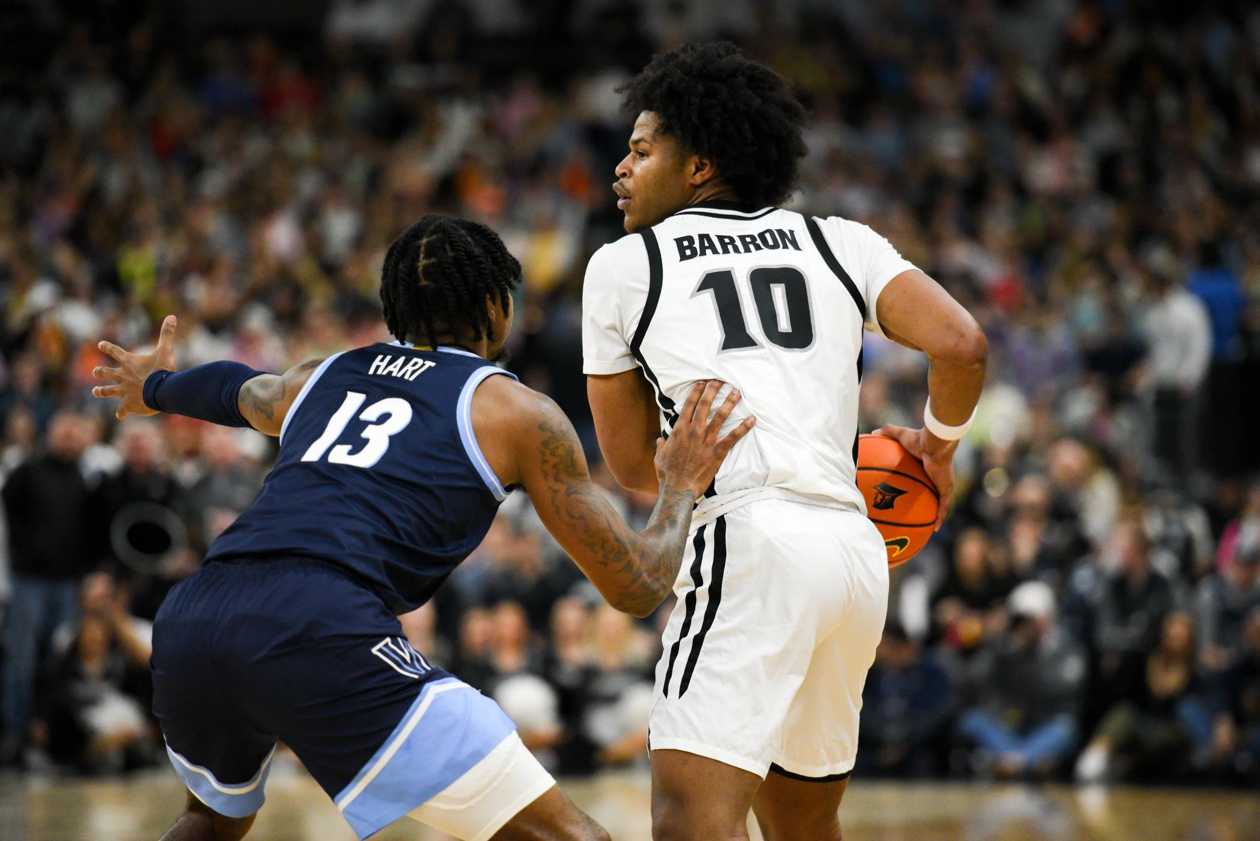 Two basketball players in a game, one in a white uniform holding a basketball, the other in a navy uniform defending.