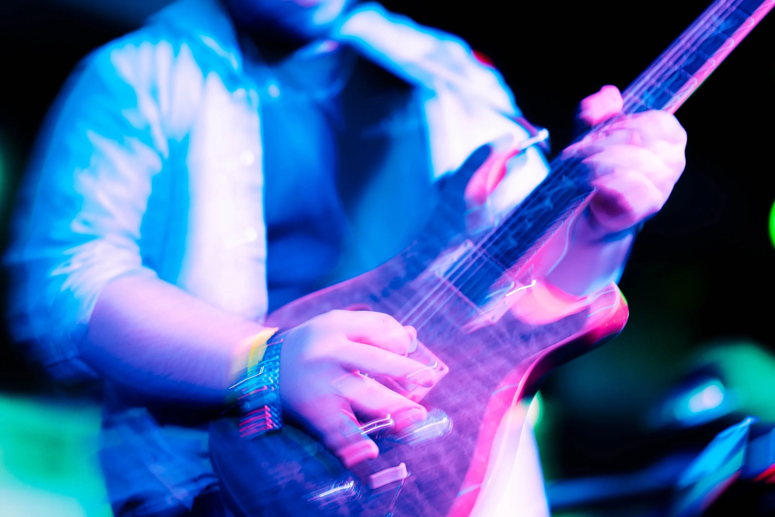 Person playing an electric guitar under colorful, neon stage lights.