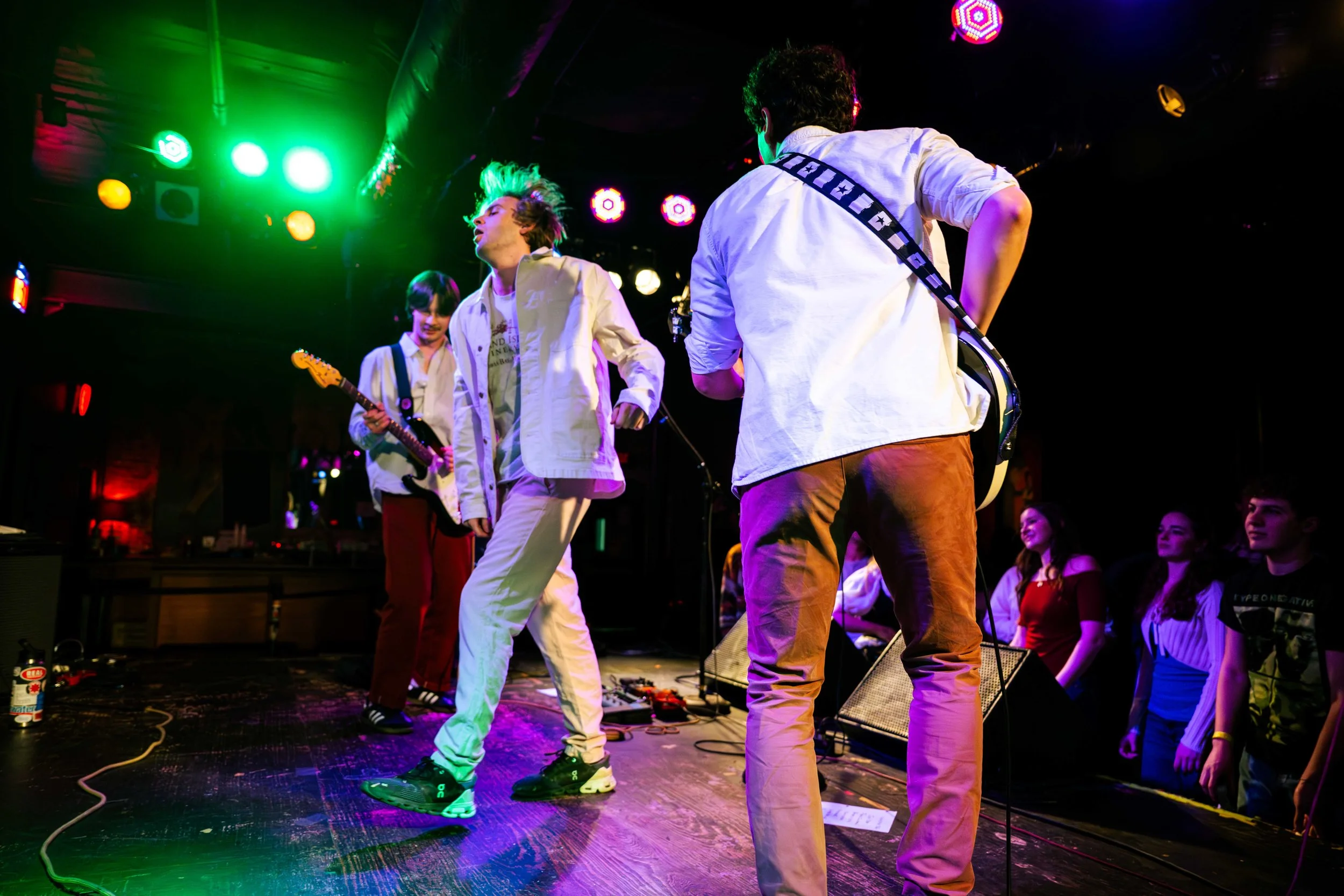 A band performing live on stage at a concert, surrounded by colorful lights and an audience watching.