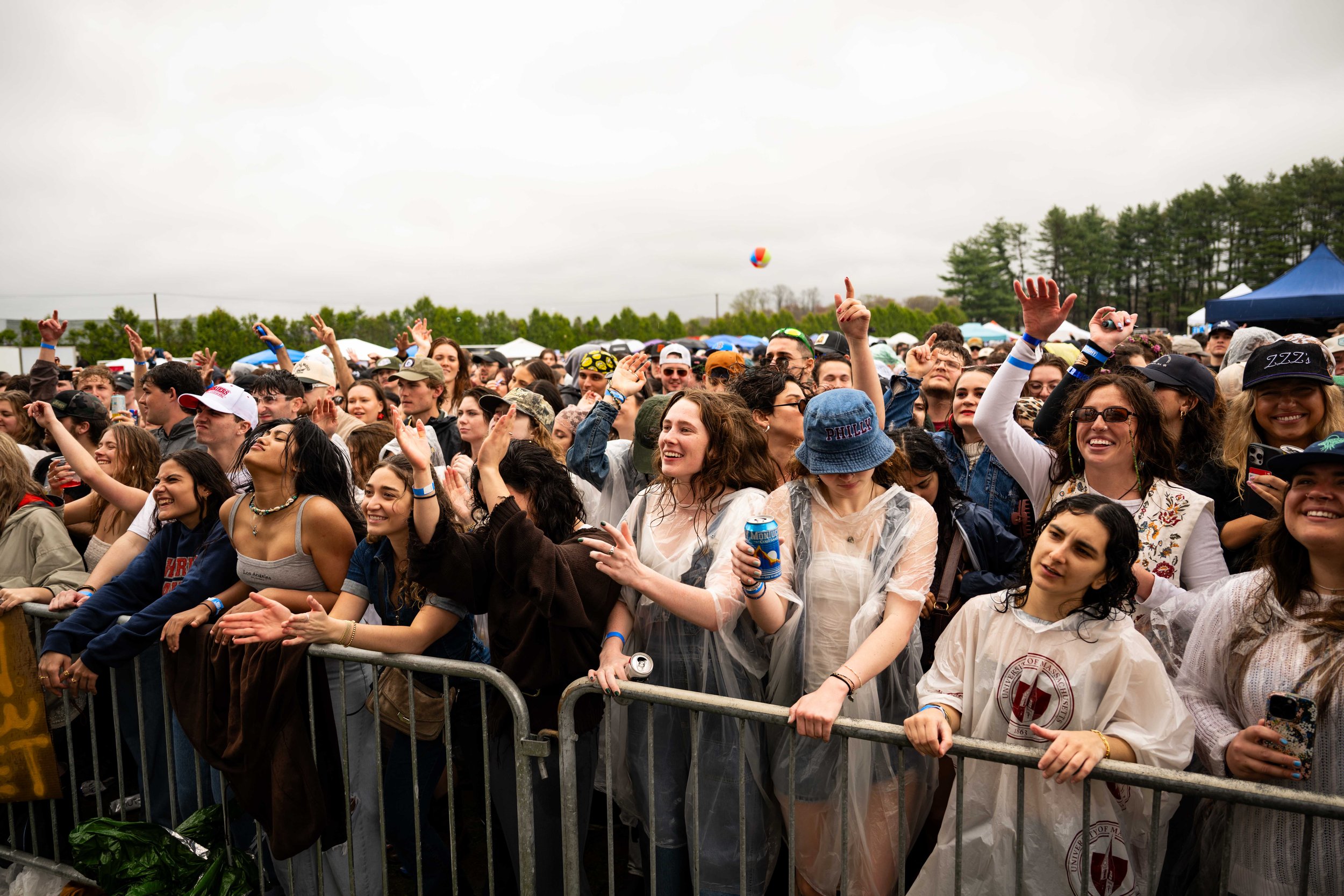 Crowd of young people enjoying outdoor concert, some dancing and smiling, with tents and trees in the background on a cloudy day.