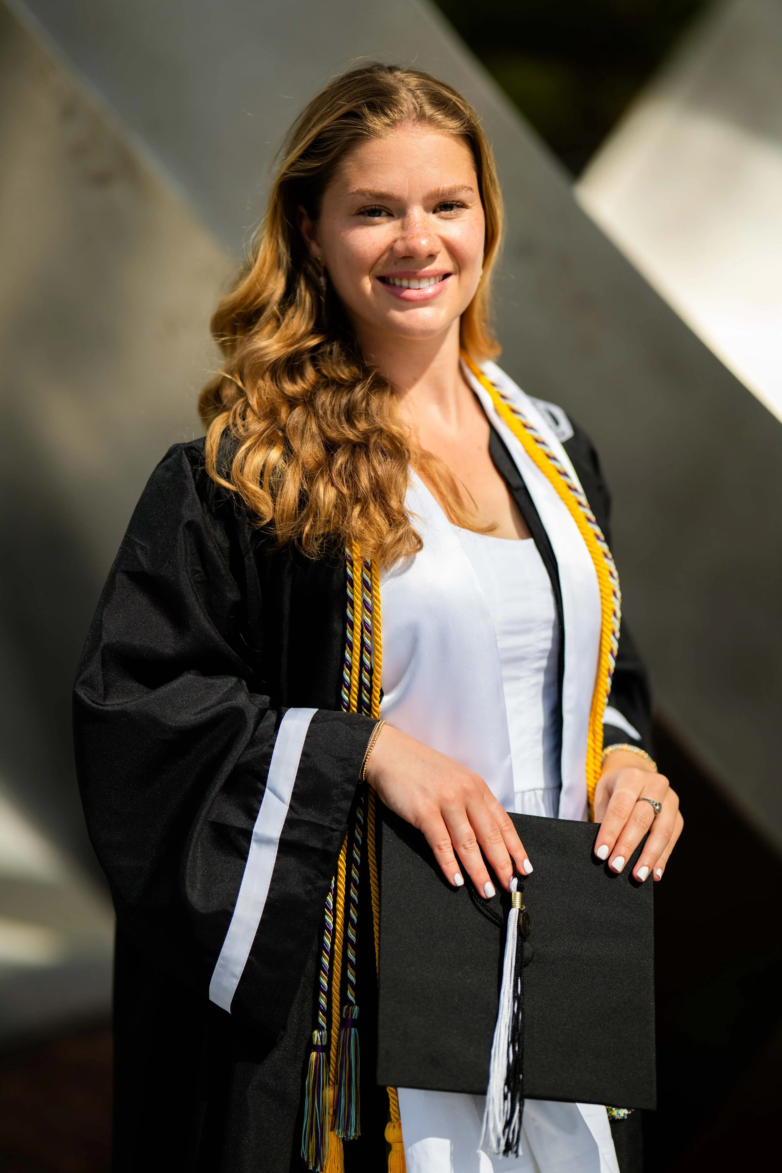 Young woman in graduation cap and gown holding diploma, smiling.