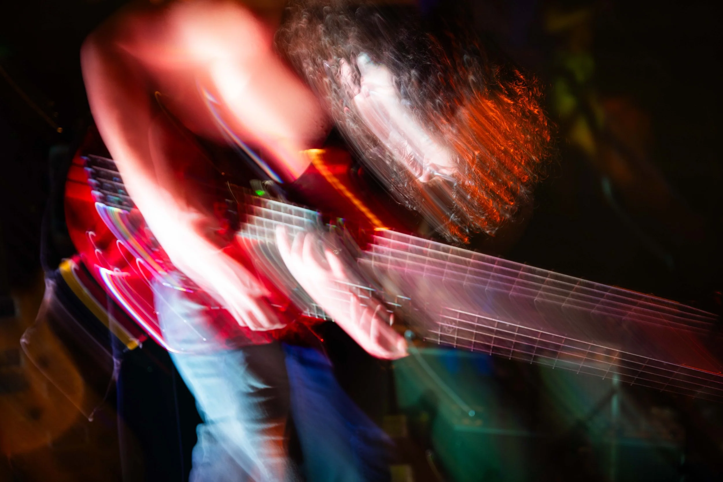 A person playing an electric guitar at night with colorful light streaks creating a blurred effect.