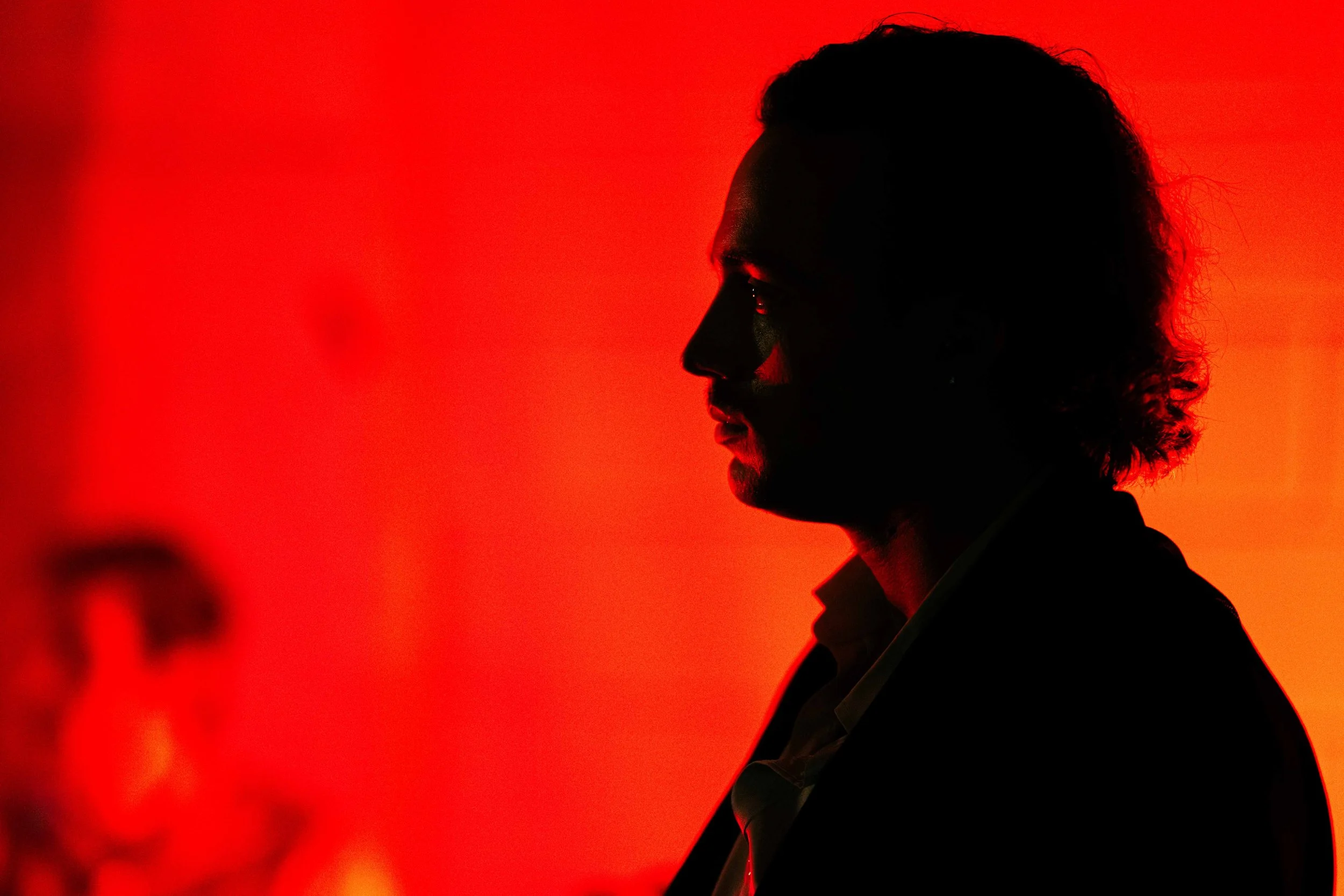 Silhouette of a man with long hair against a red background.