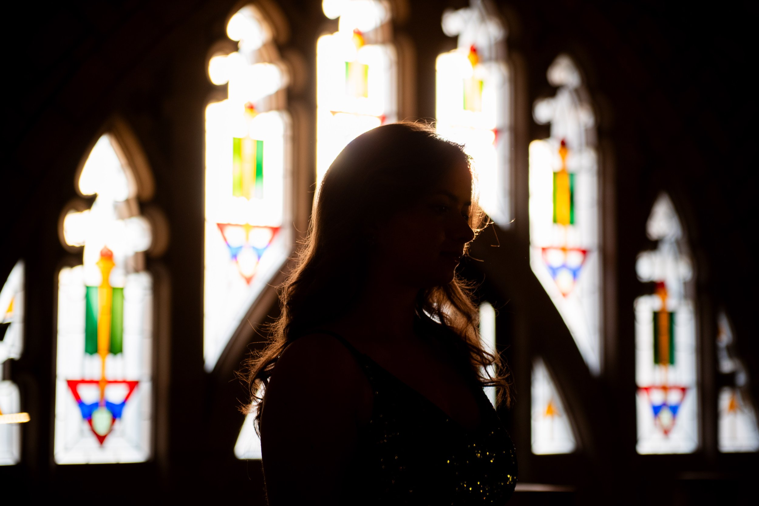 Silhouette of a woman inside a church with stained glass windows in the background.
