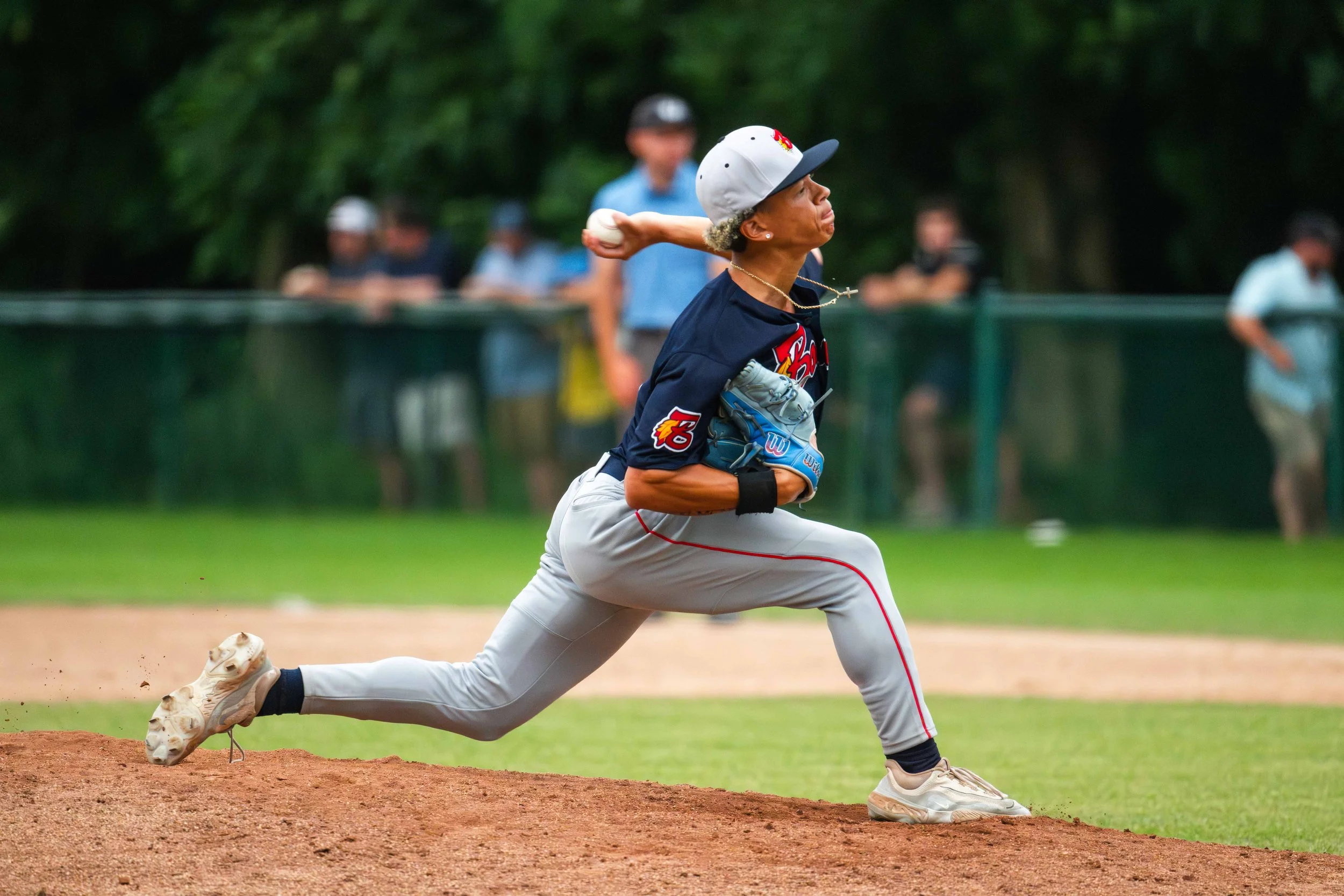 A man  in baseball attire, including a gray cap, navy shirt, gray pants, and beige shoes, is throwing a baseball on a baseball field.  