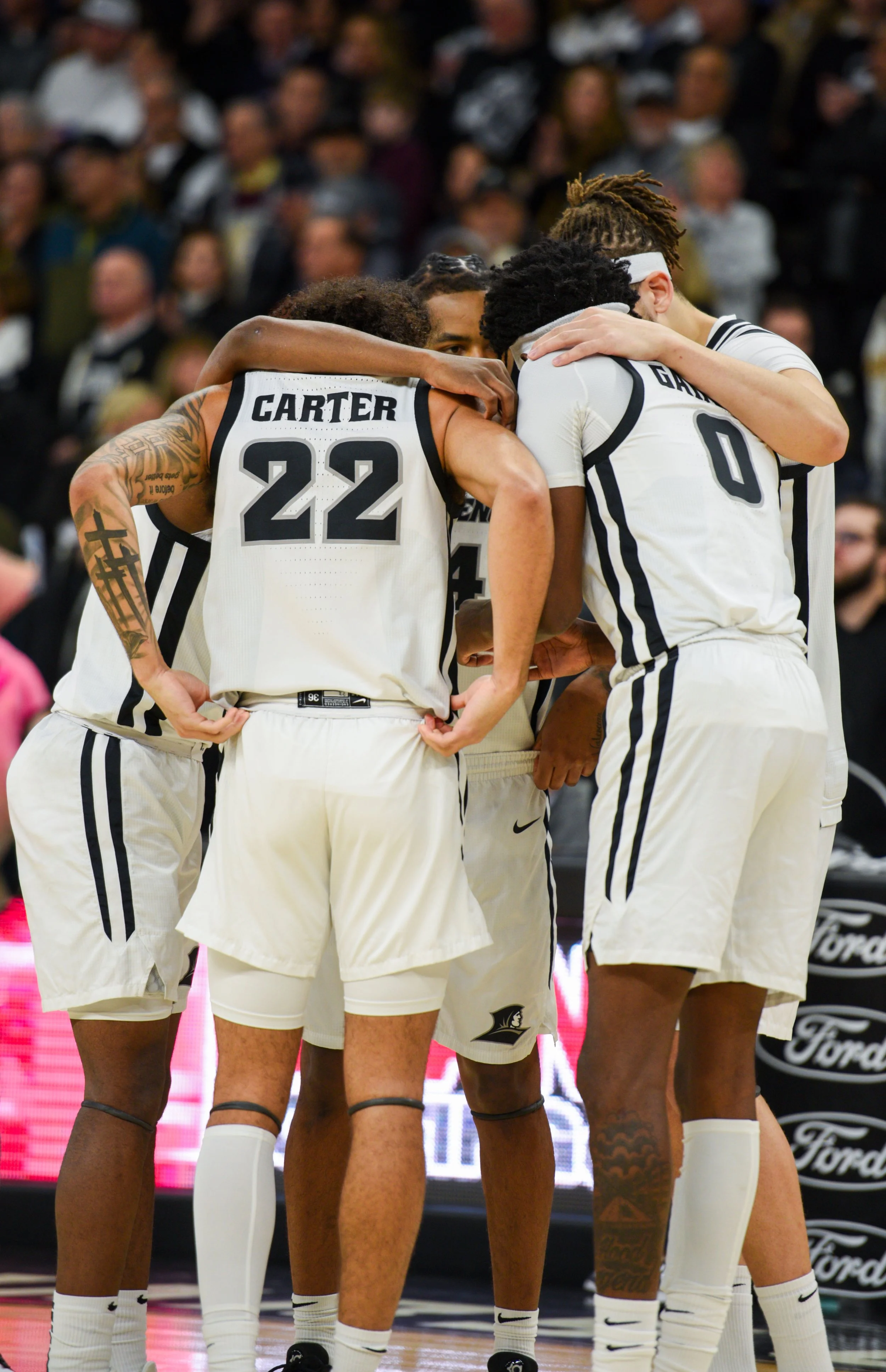 A group of basketball players wearing white jerseys with black stripes huddled together on the court during a game.