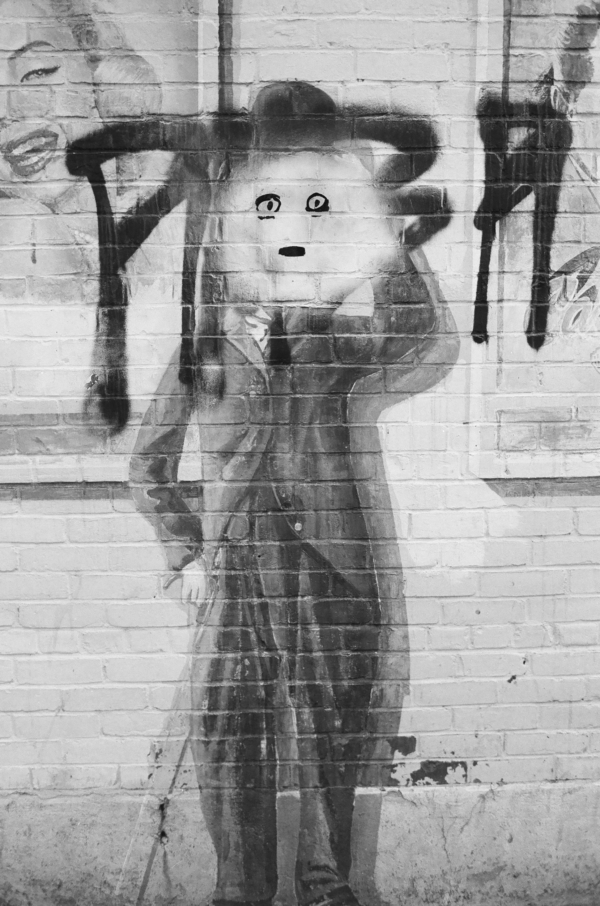 Black and white mural of a young girl with a pig face, holding a baseball bat over her shoulder, with a background of a brick wall.