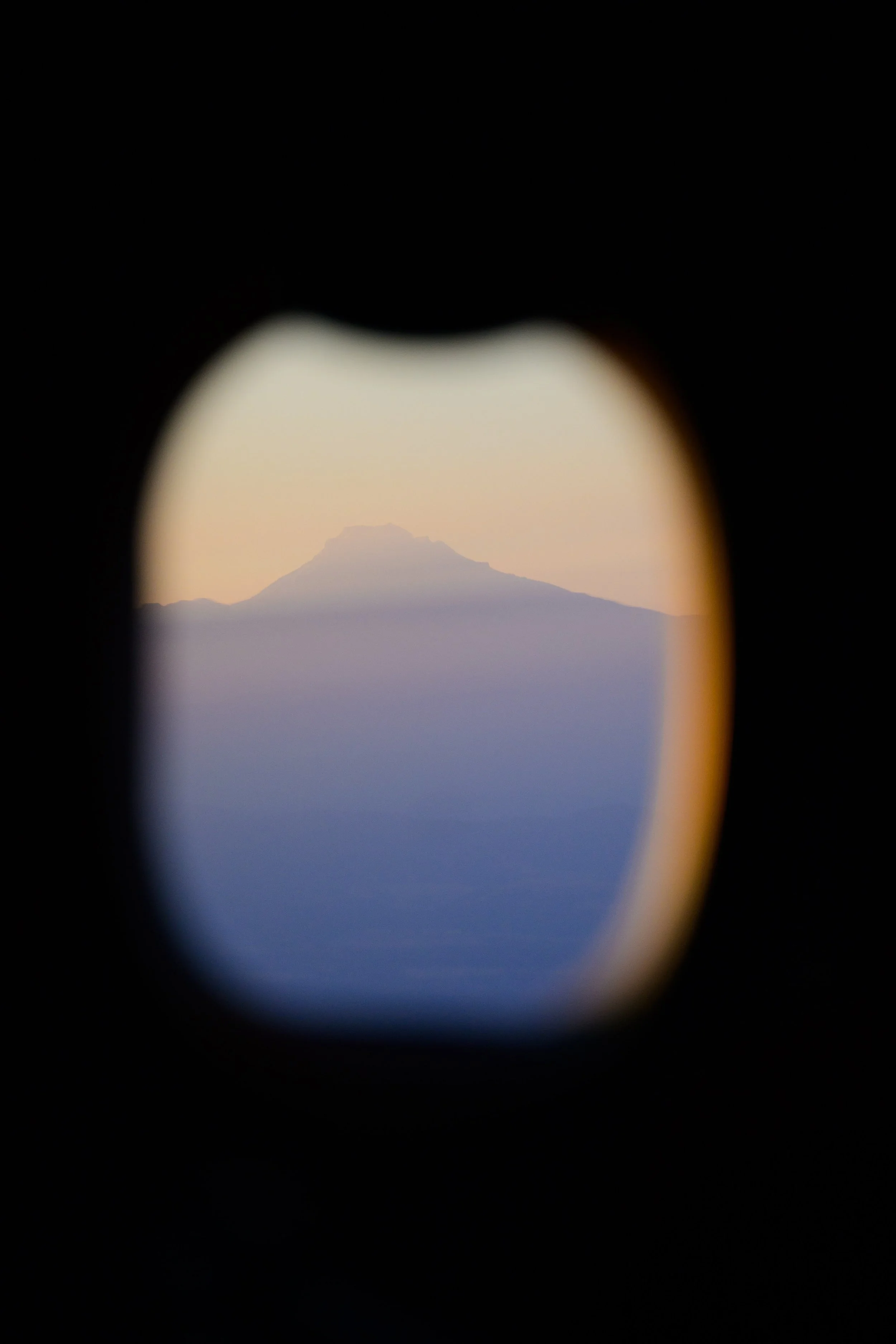 View of a mountain through an aircraft window with an irregular shape, suggesting it was taken from an airplane.
