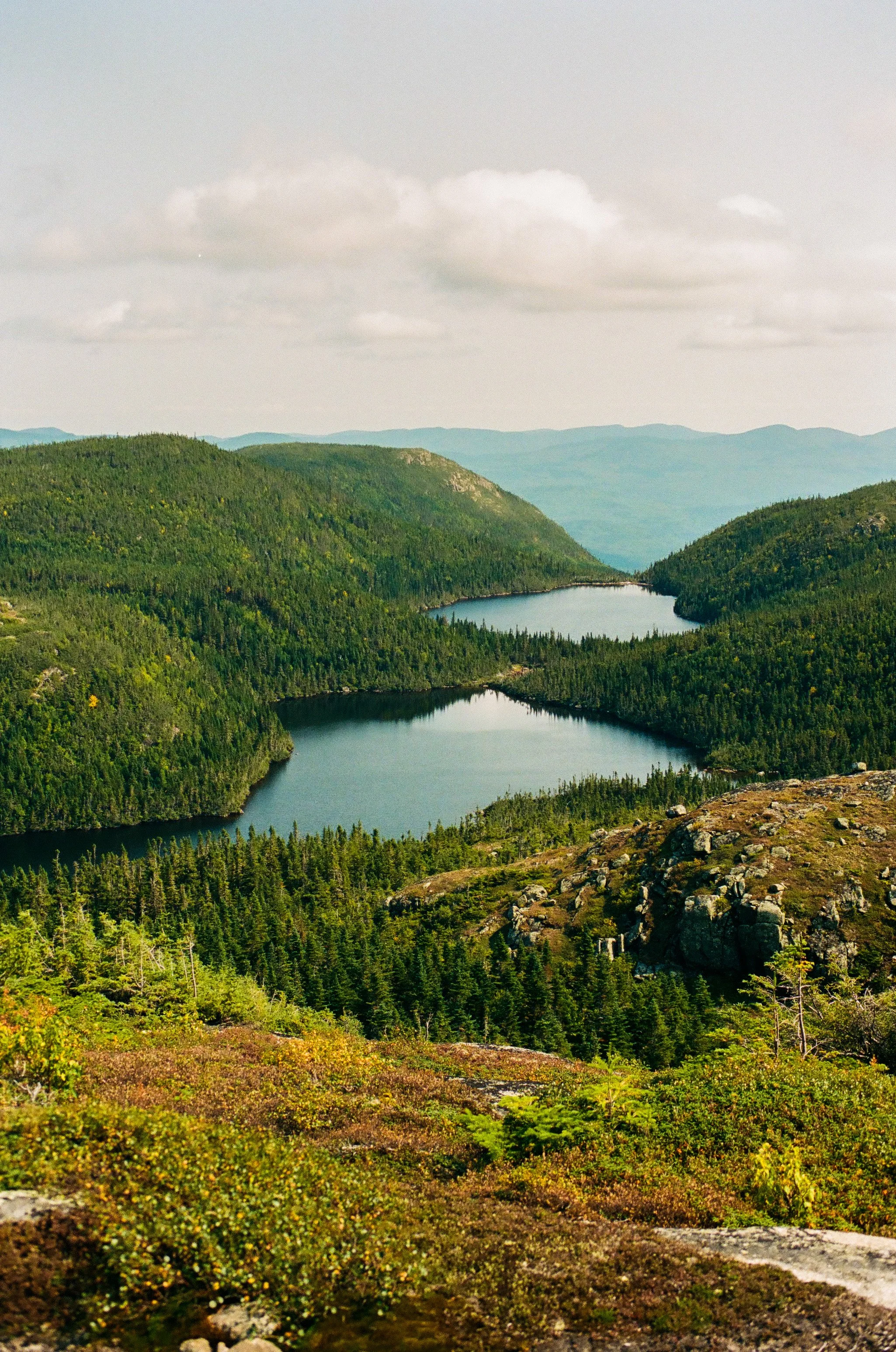 Scenic view of a mountain landscape with two lakes surrounded by dense green forests and a cloudy sky.